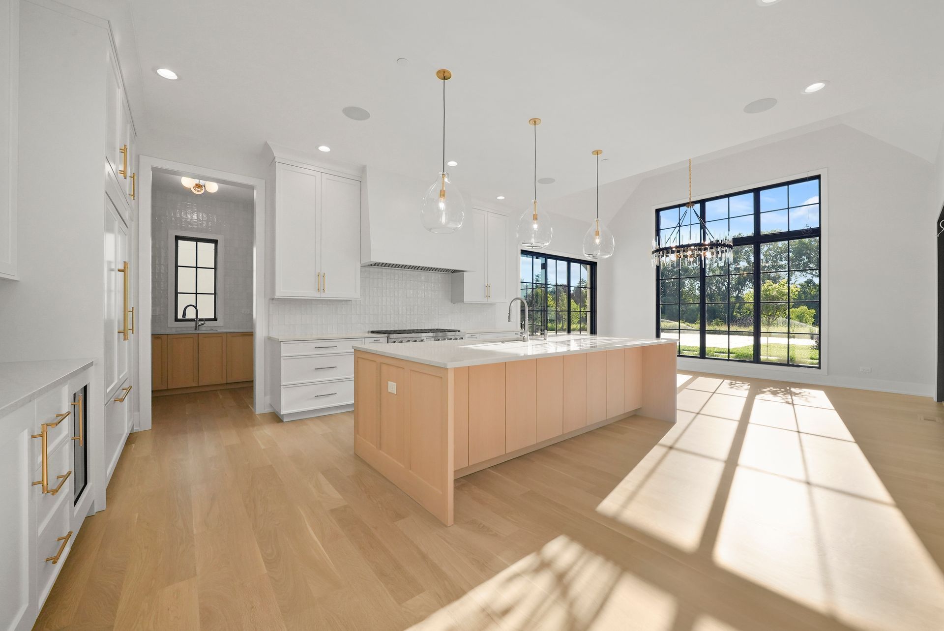 Bright modern kitchen with white cabinets, wood island, and large windows letting in sunlight.