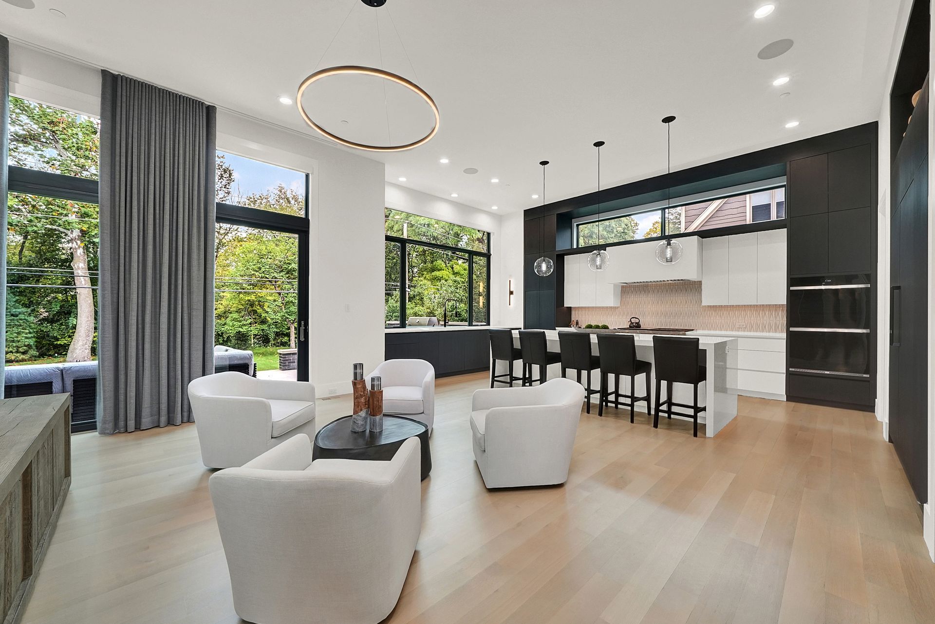 Bright open-plan living room and kitchen with modern furniture, large windows, and light wood floors