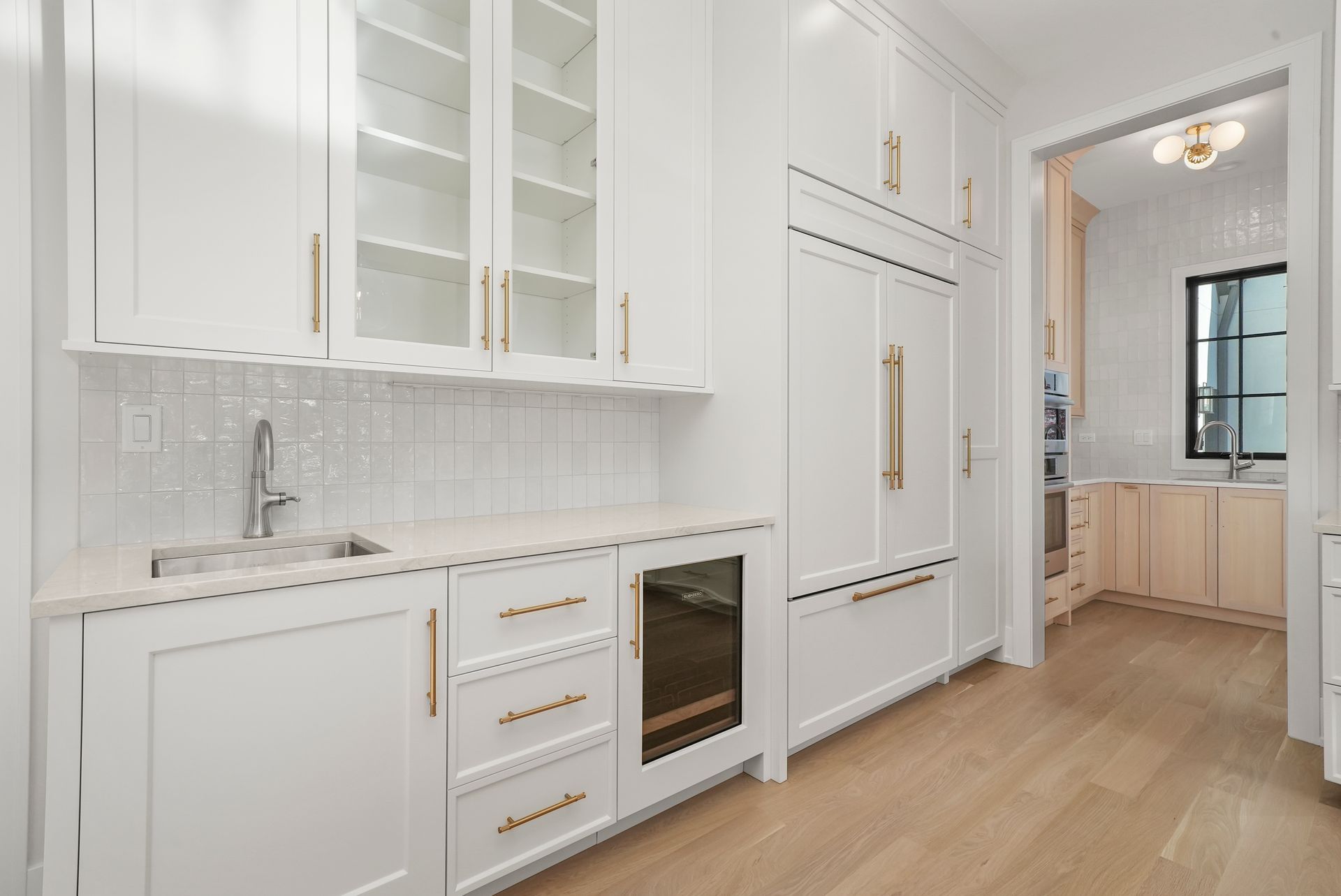 Bright white galley kitchen with gold hardware, wood floors, and built-in oven and refrigerator