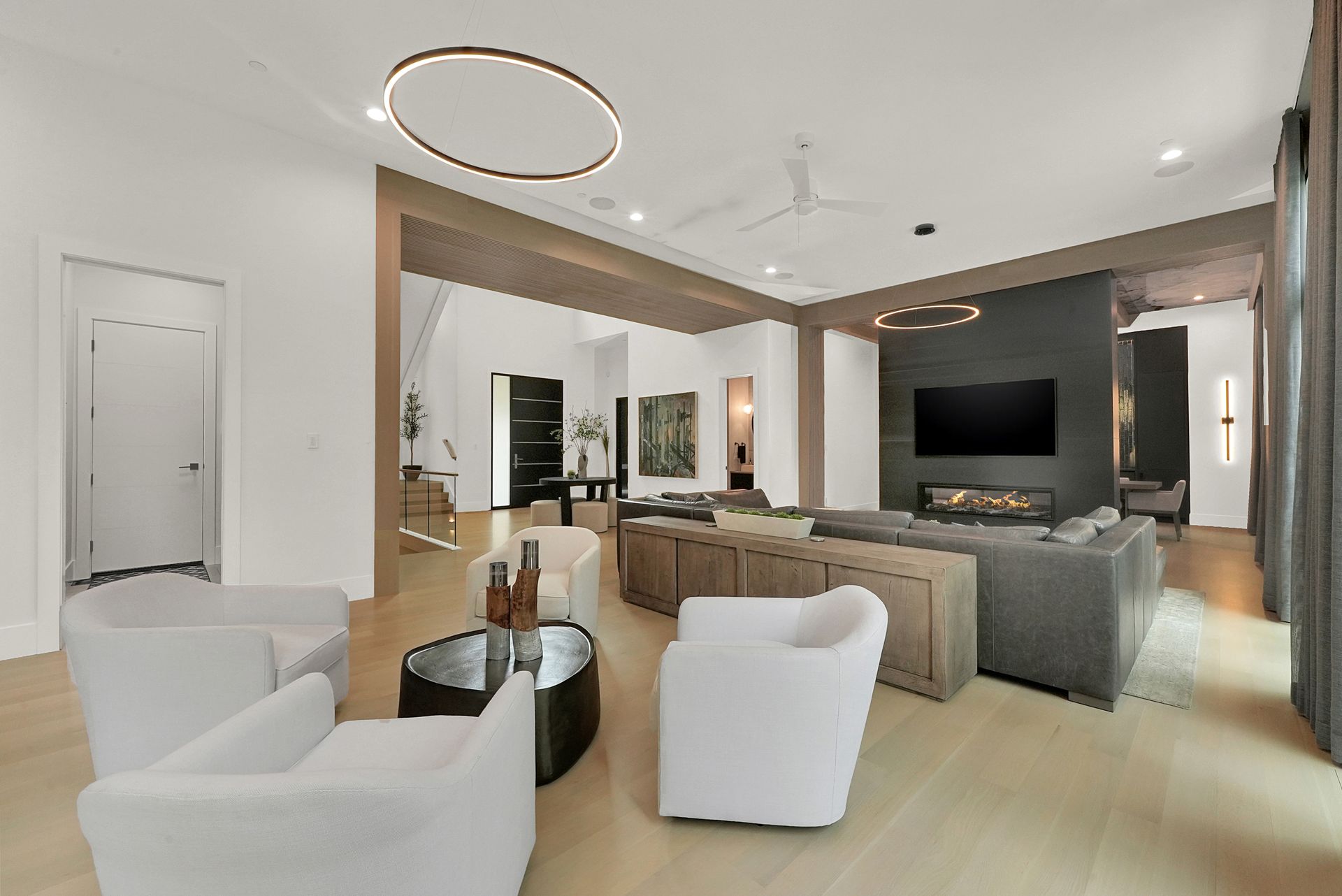 Modern open-plan living room with neutral decor, white chairs, beige sofas, and a wall-mounted TV