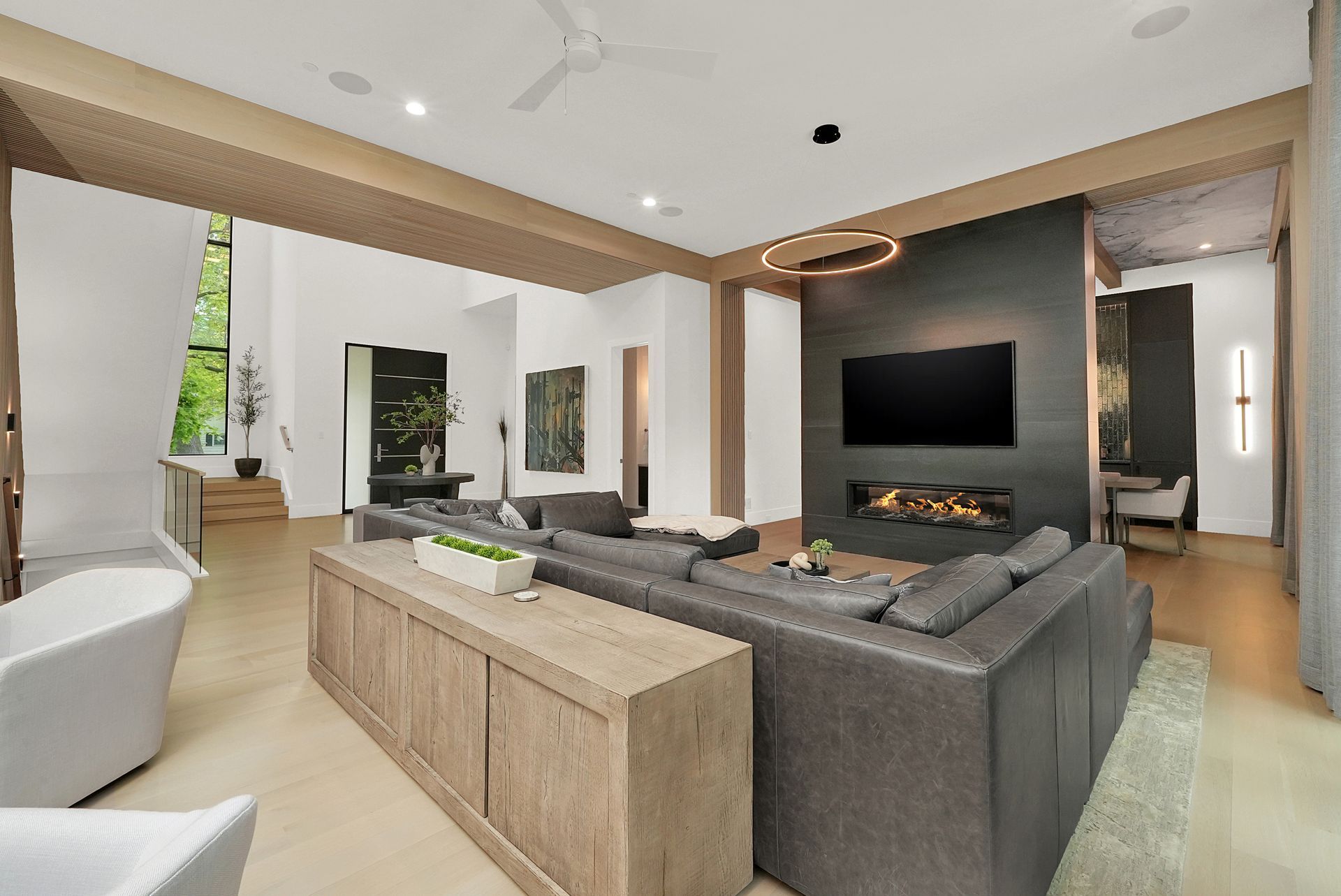 Modern living room with gray sectional, wall-mounted TV, and wood accents, opening to an outdoor view