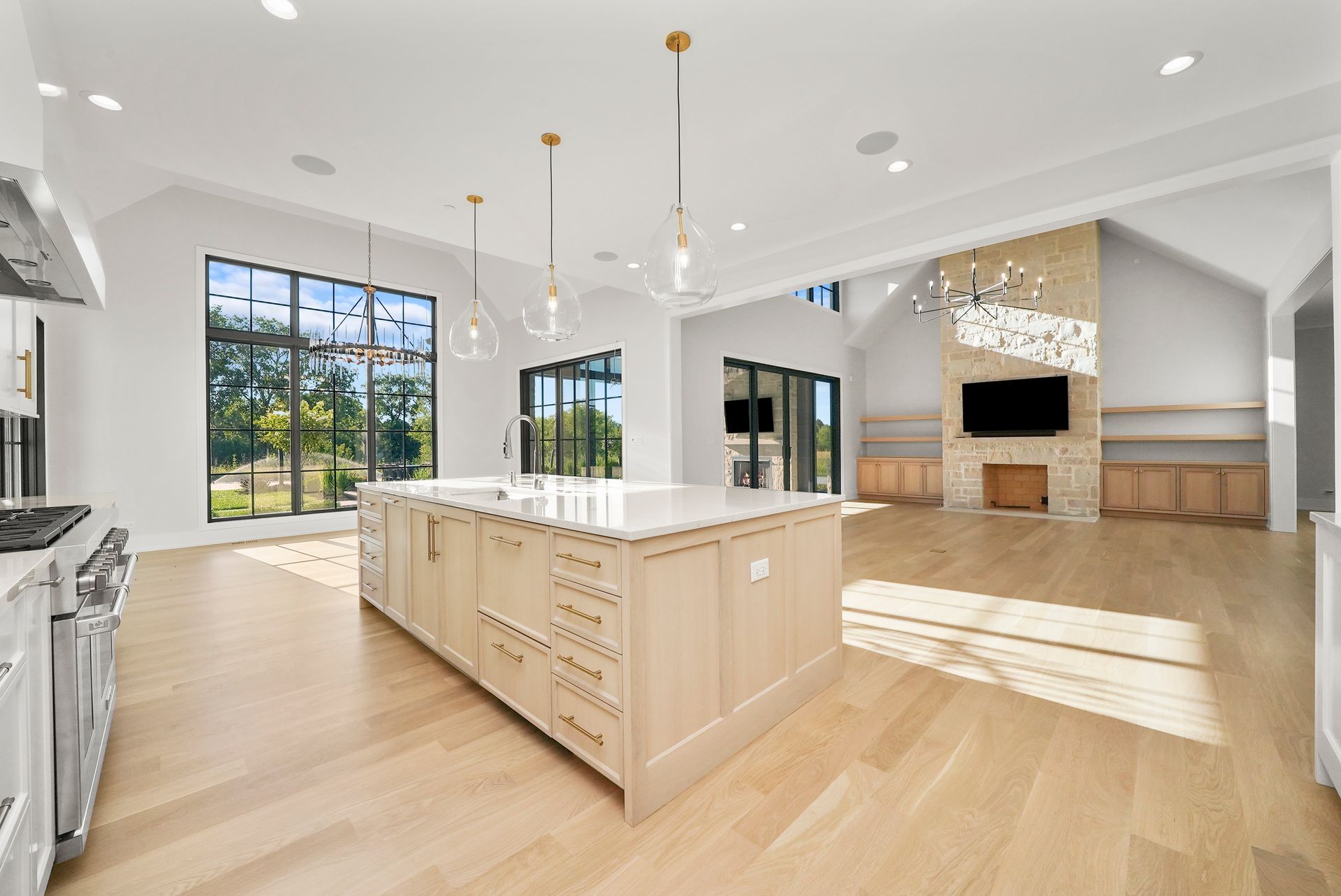 Bright open-plan kitchen and living room with white island, light wood floors, and a fireplace.