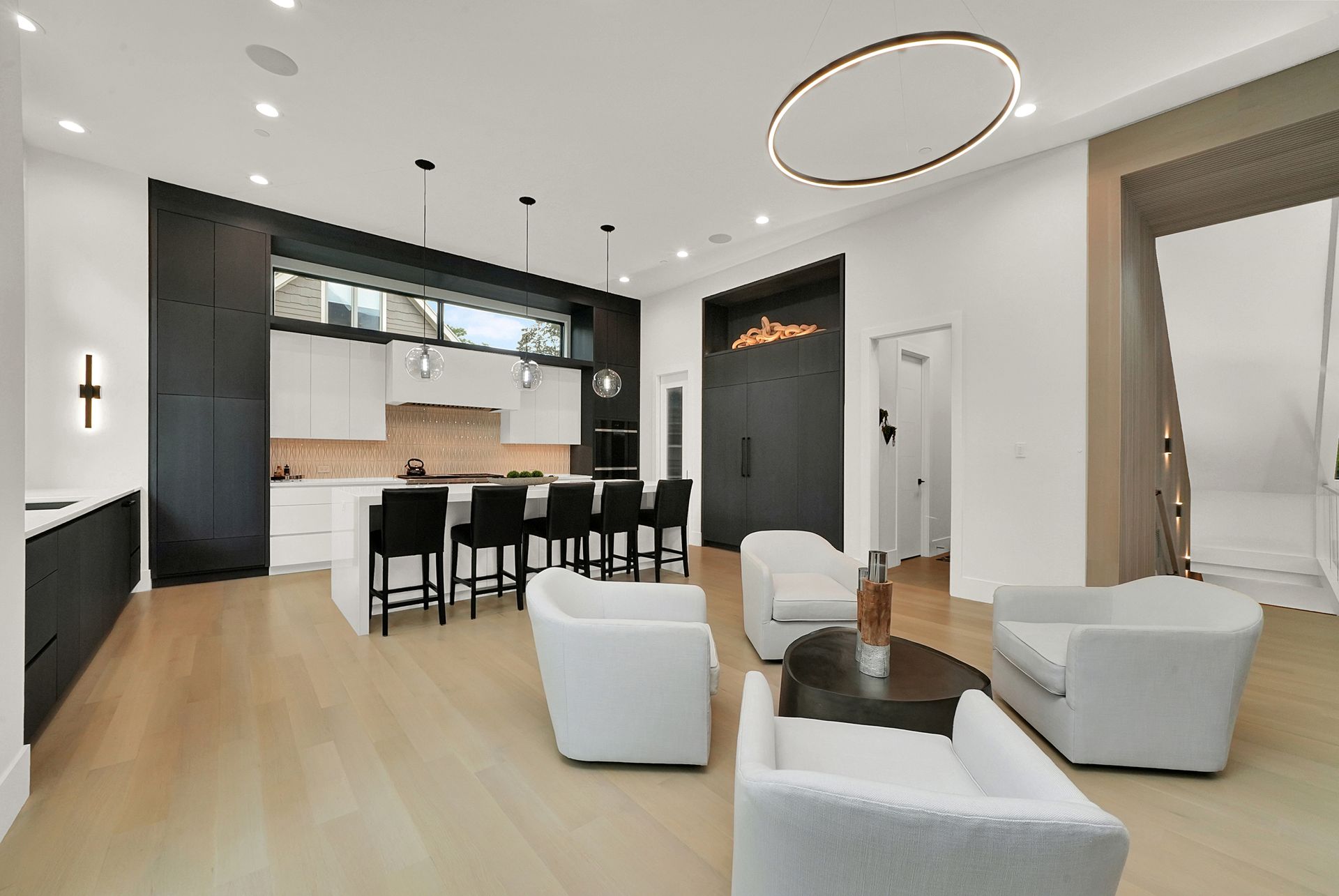 Modern open-concept living room and kitchen with light wood floors, white chairs, and black cabinetry