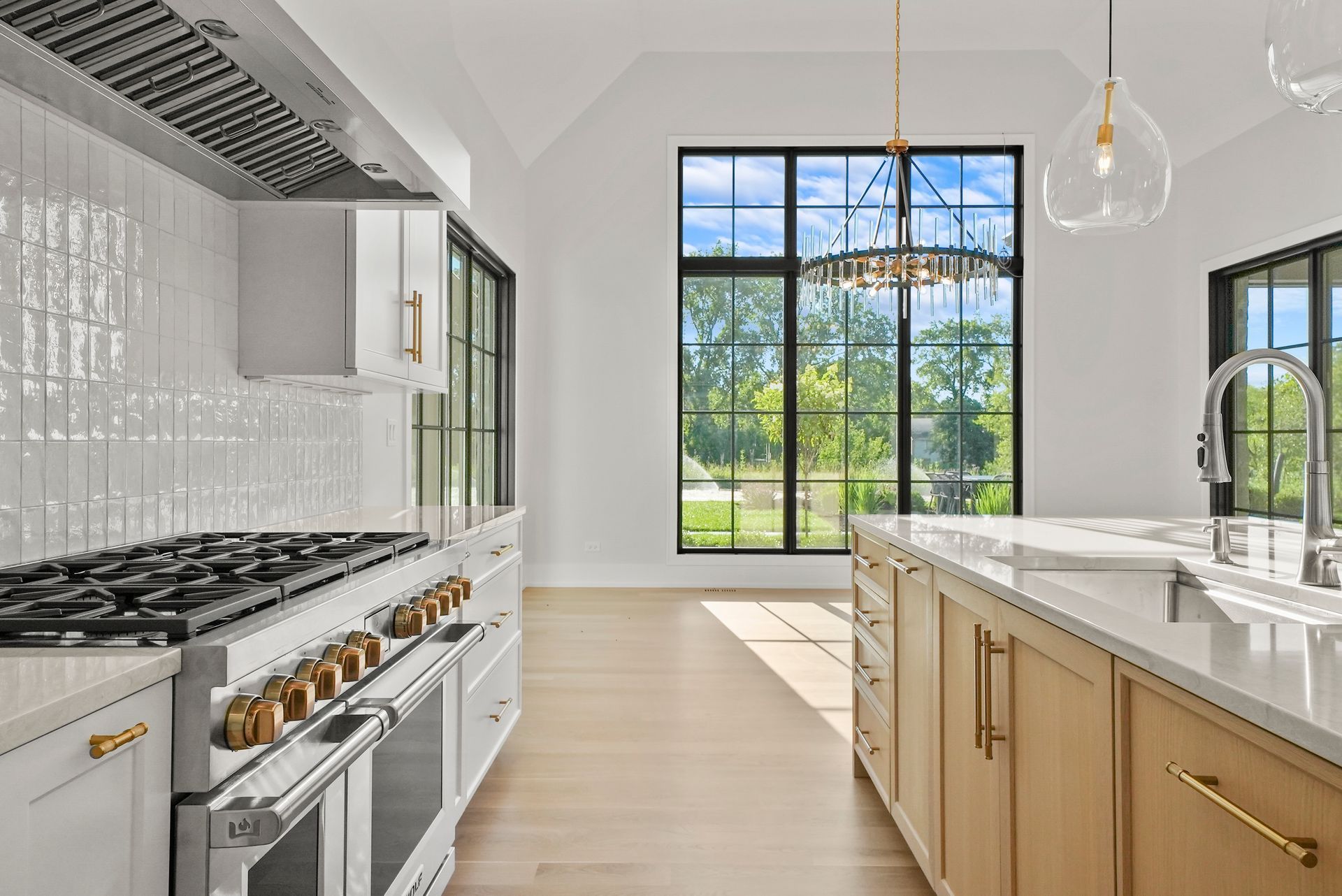 Bright modern kitchen with white cabinets, marble island, and large black-framed window overlooking a green yard