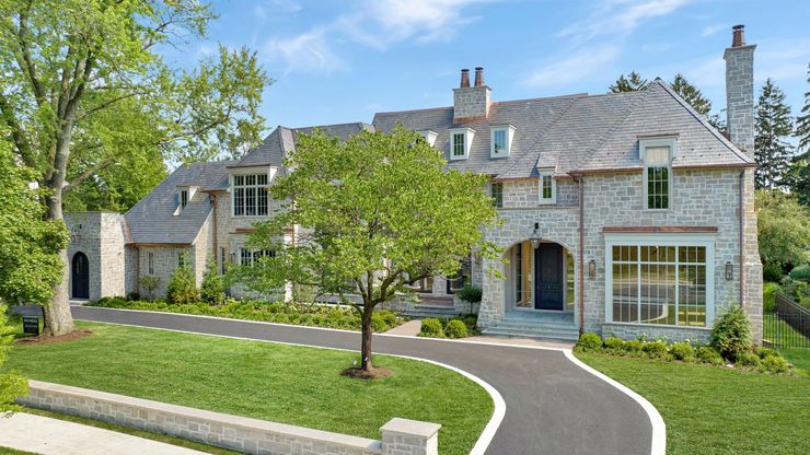A large white house with a black roof is sitting on top of a lush green hillside.