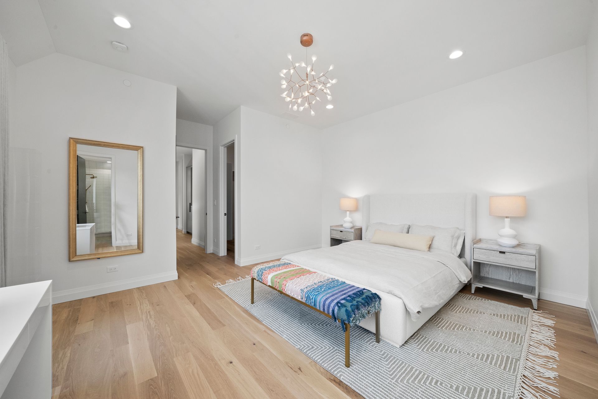 Bright white bedroom with twin beds, wood floors, and a chandelier in a minimalist interior.