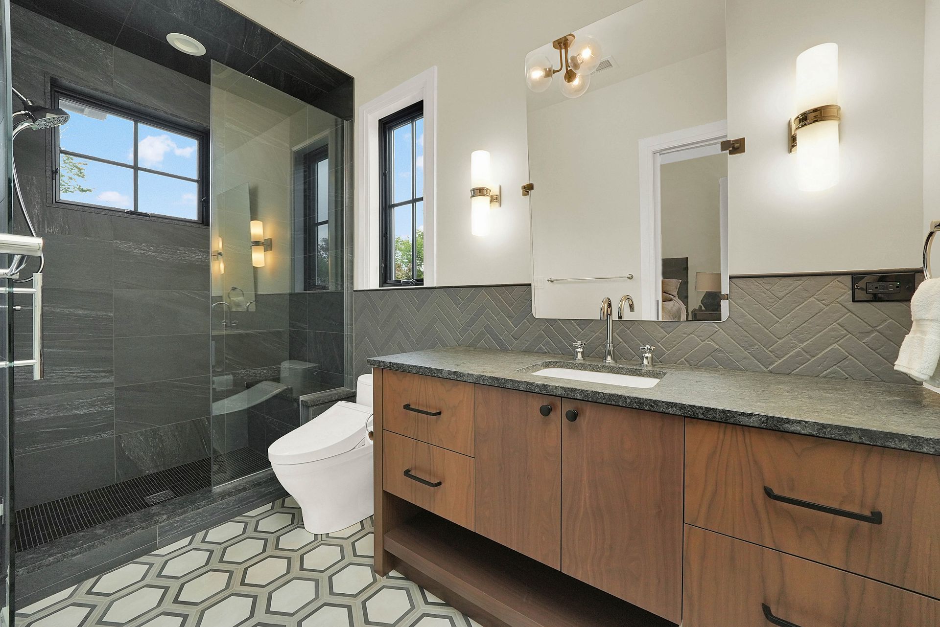 Modern bathroom with gray tiled shower, white toilet, and wood vanity with granite countertop