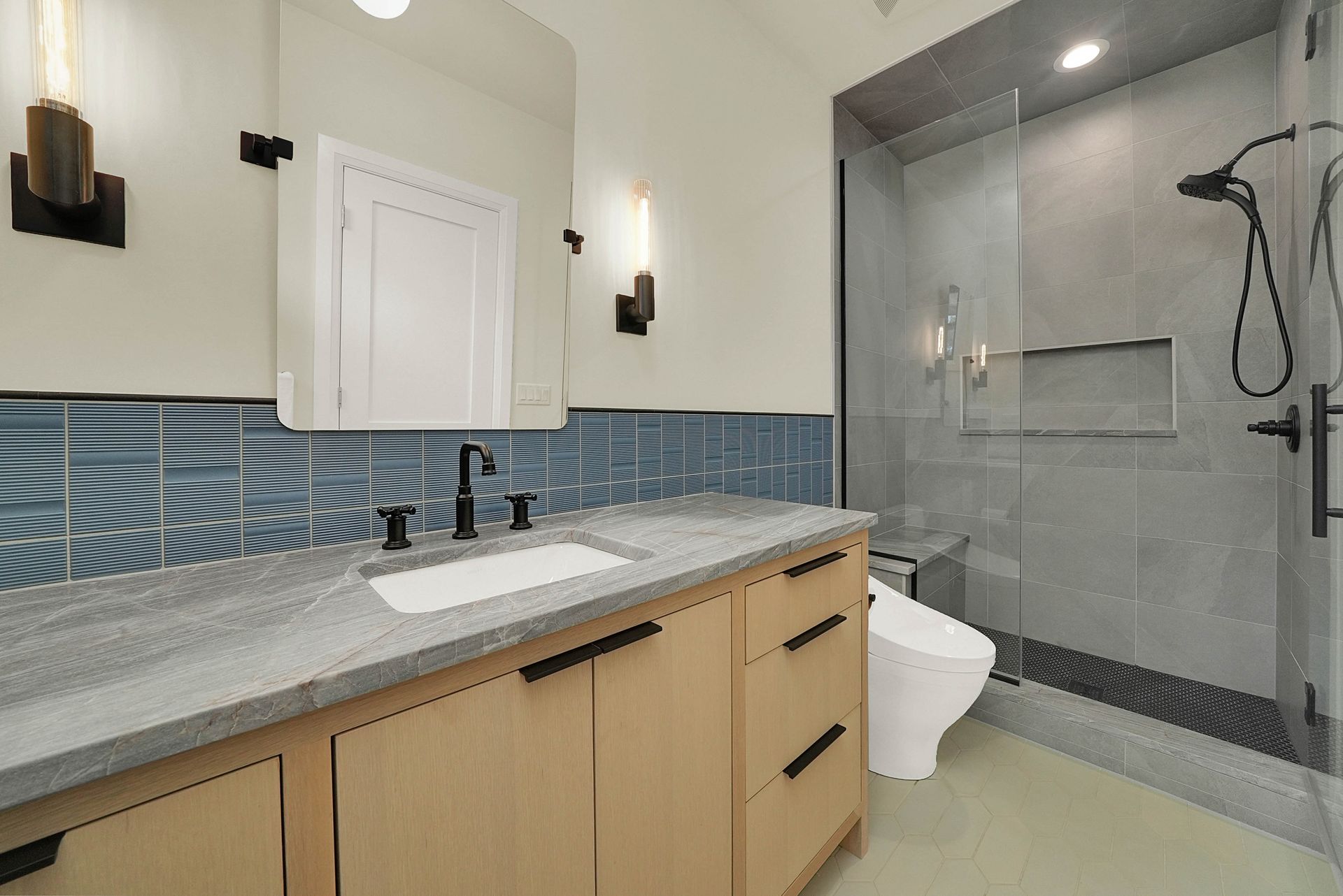 Modern bathroom with wood vanity, blue tile backsplash, and glass shower enclosure