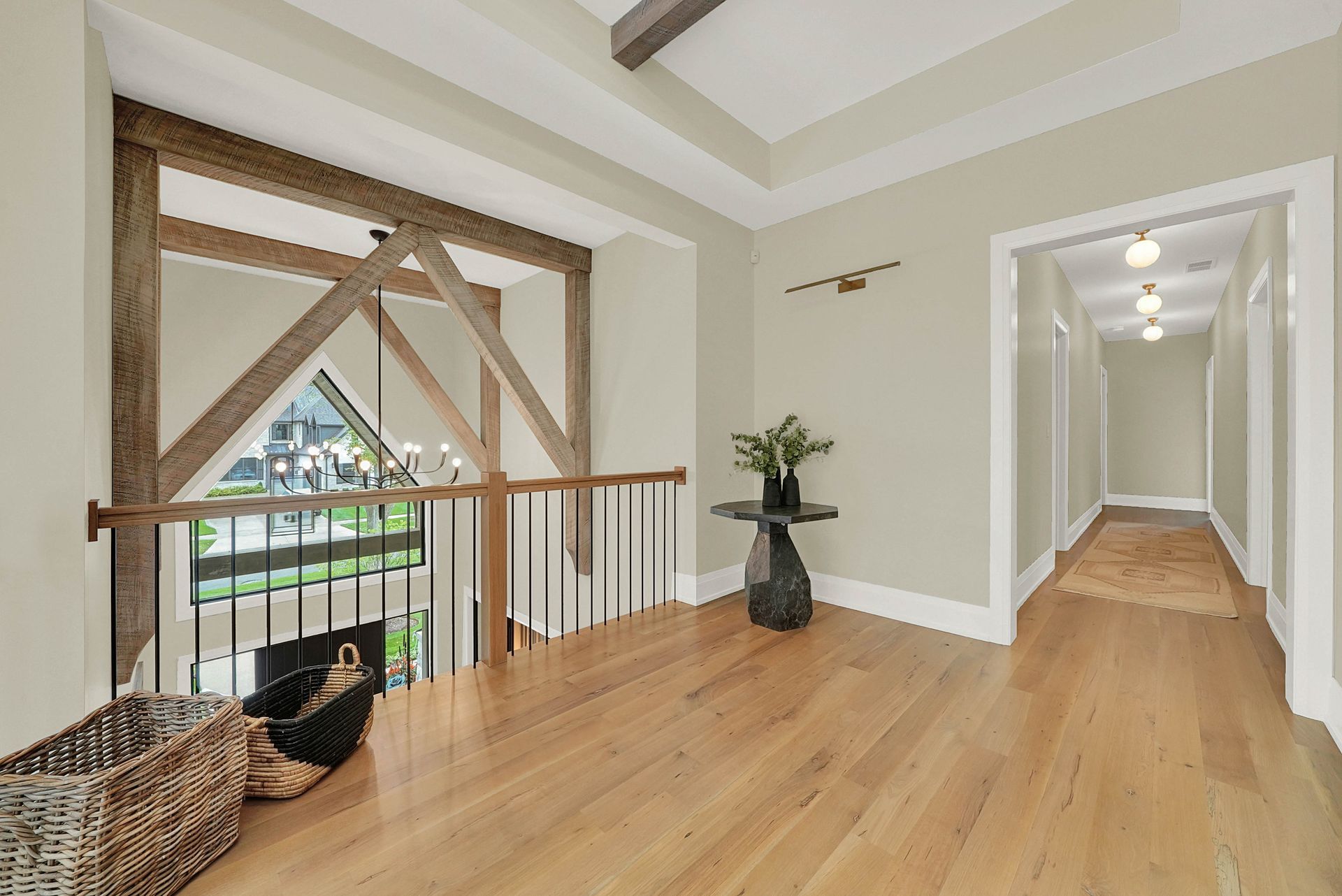 Bright hallway with wood floors, exposed beams, railing, and a potted plant beside a long corridor