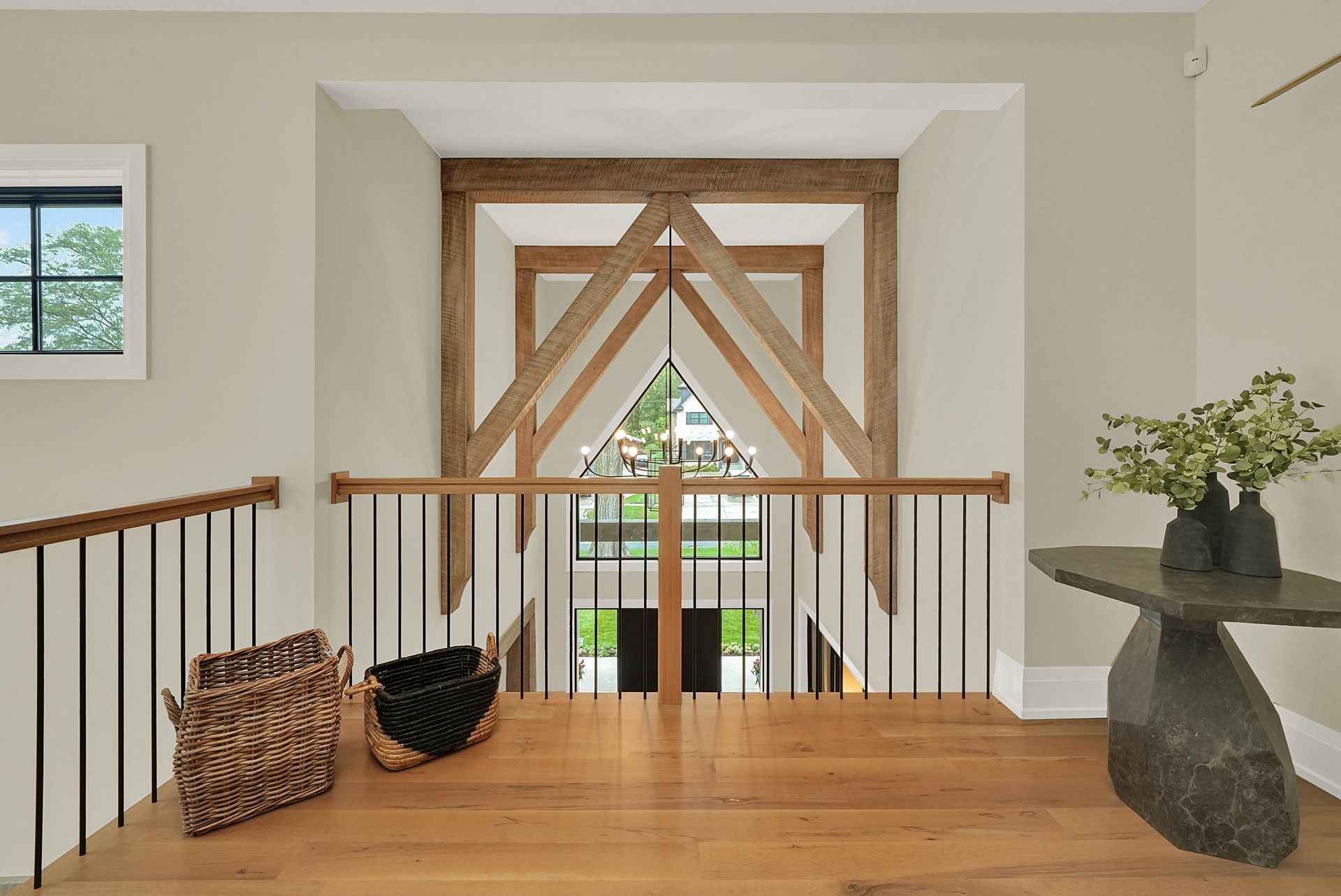Bright upstairs landing with wooden floor, railing, woven baskets, and a large windowed doorway with wood braces