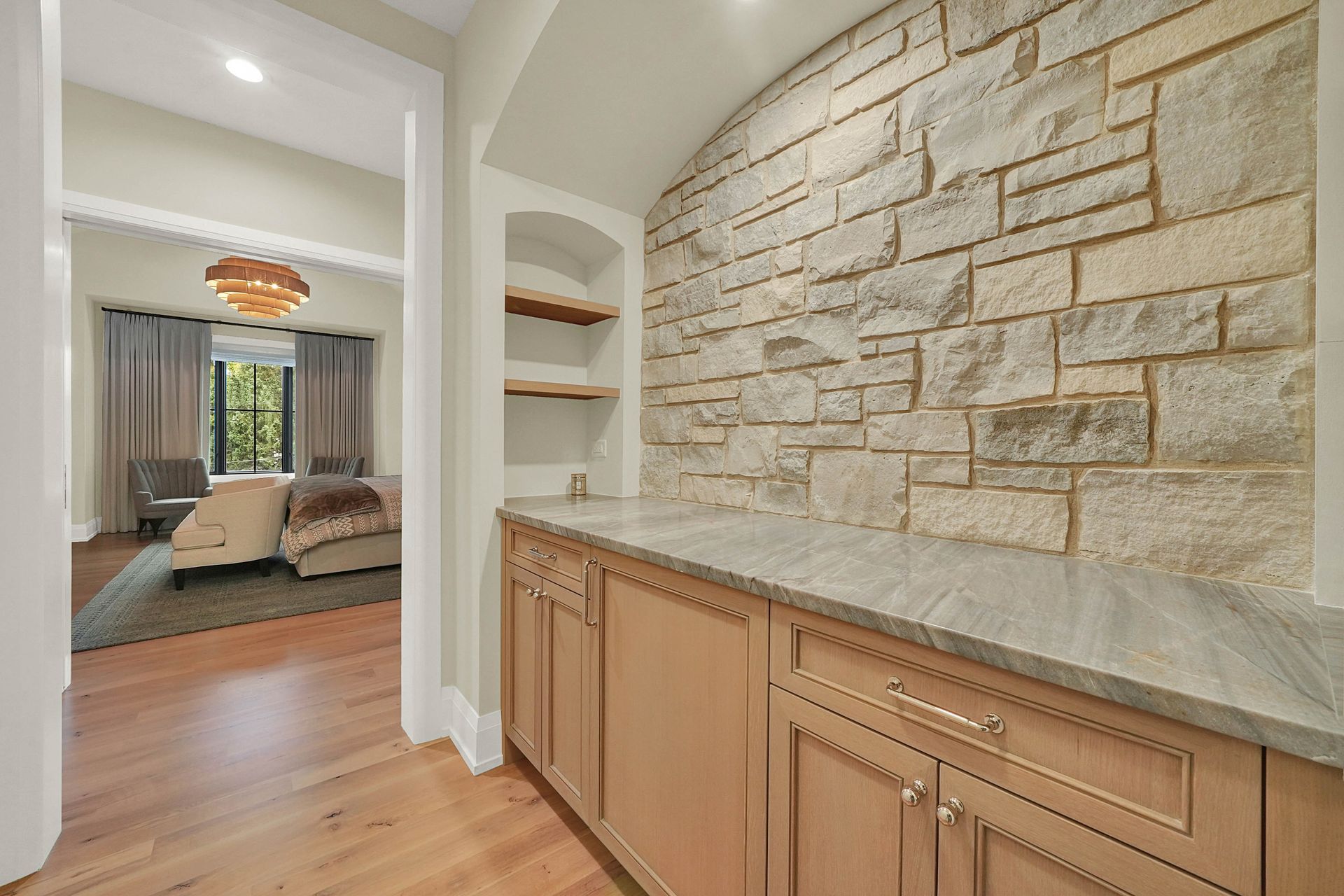 Hallway with stone accent wall, built-in cabinets, and view into a bedroom with a hanging light fixture.