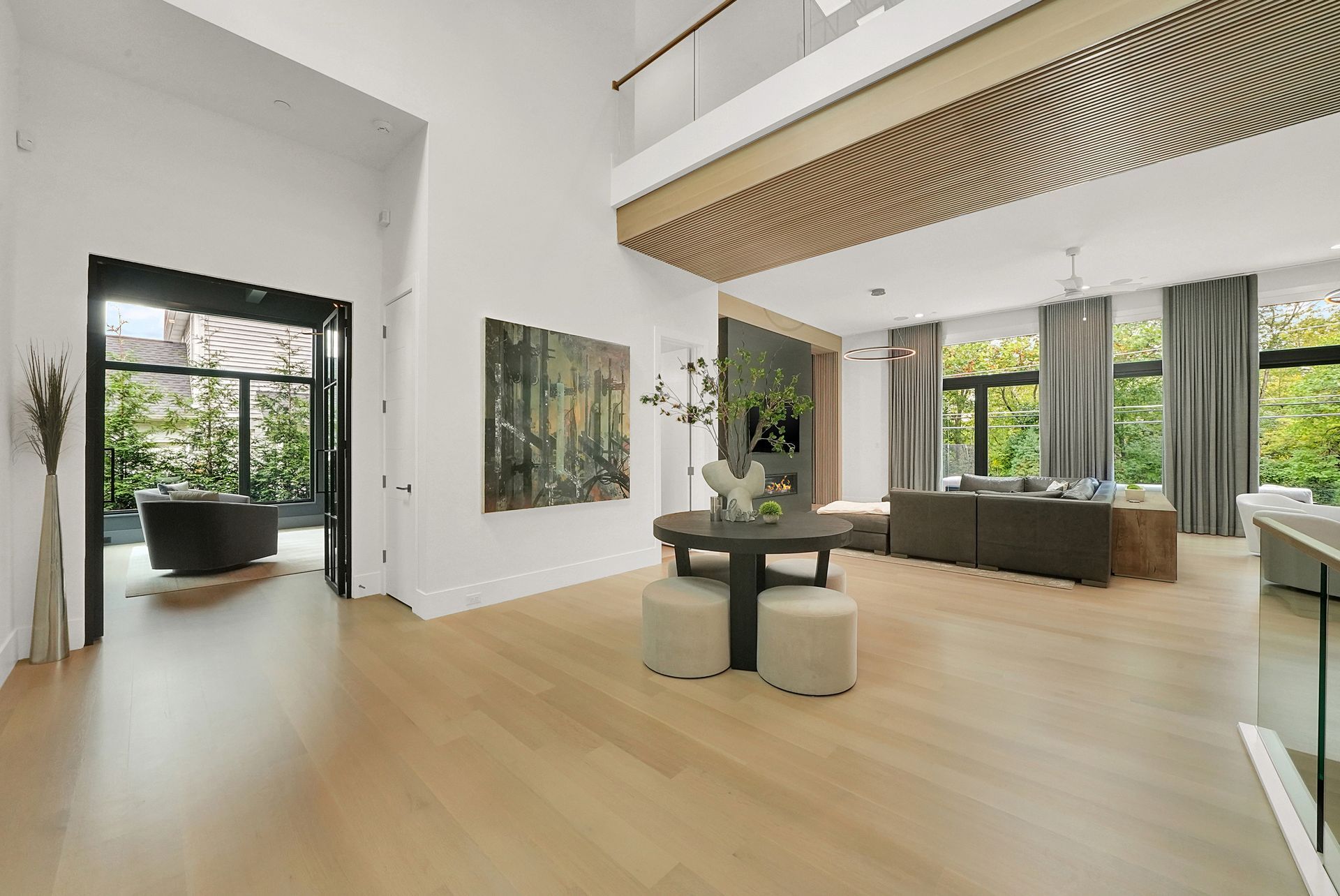 Bright modern living room with light wood floors, tall windows, a sofa, and decorative wall art