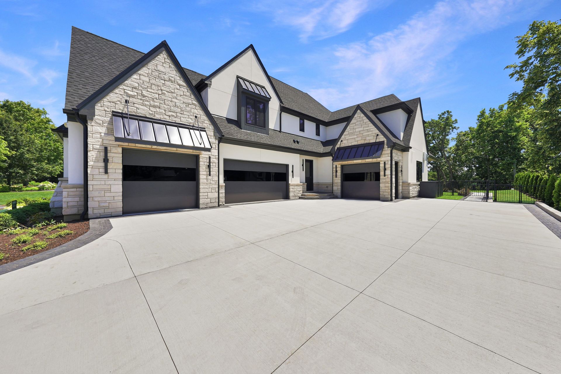 Large stone-and-gray suburban house with three garage doors and a wide concrete driveway under a blue sky