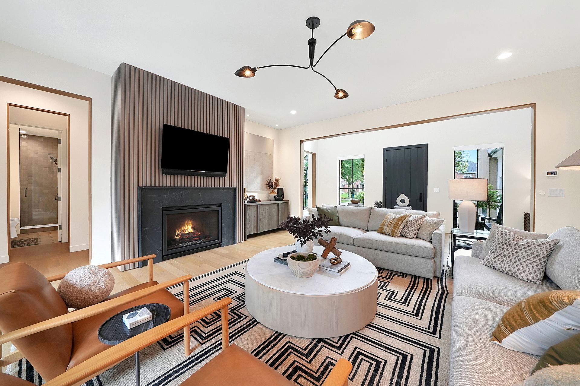 Modern living room with fireplace, TV, sectional sofa, round ottoman, and black-and-white geometric rug
