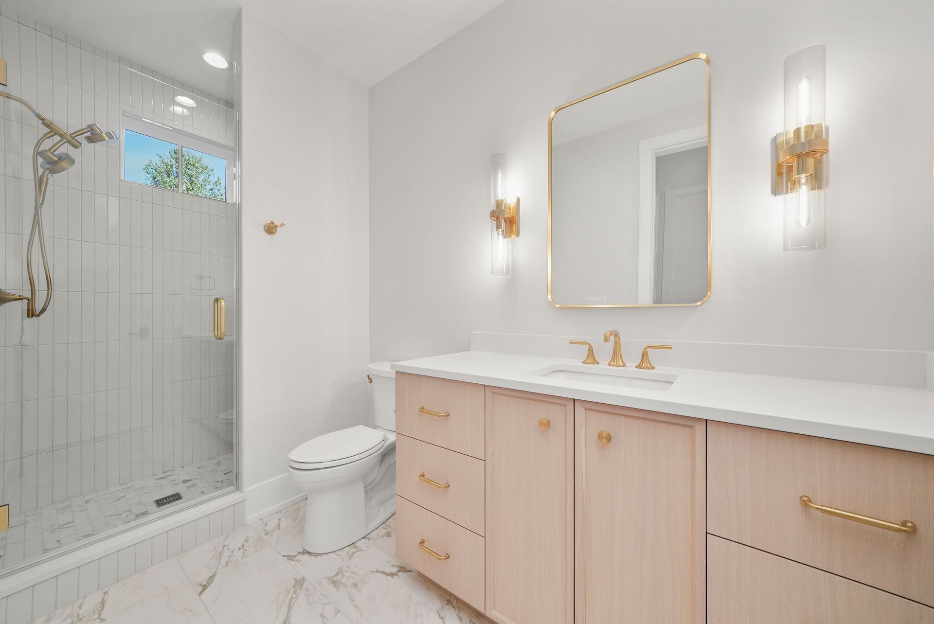 Bright white bathroom with glass shower, gold fixtures, floating vanity, and large mirror