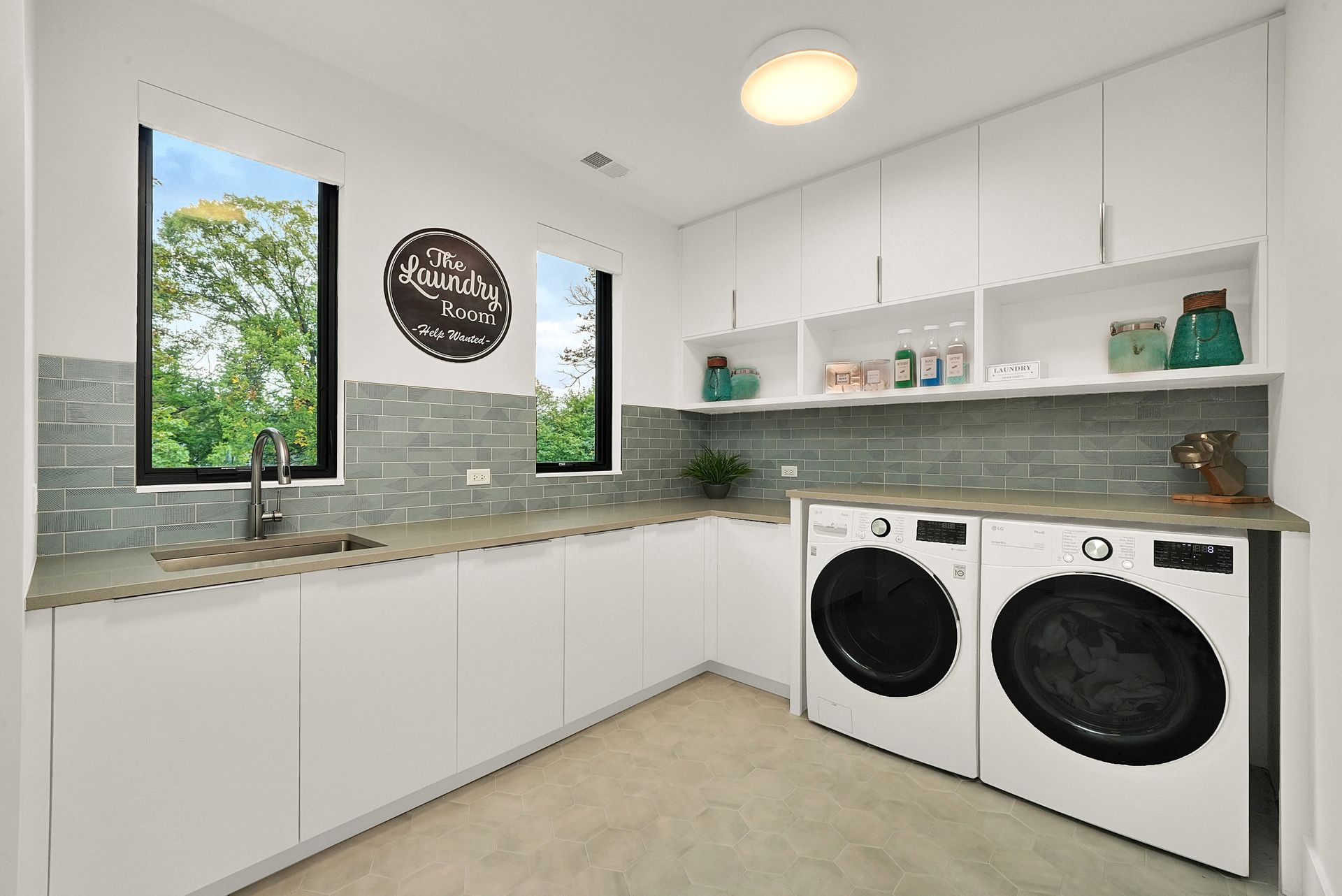 Bright laundry room with white cabinets, gray tile backsplash, sink, and front-loading washer and dryer.