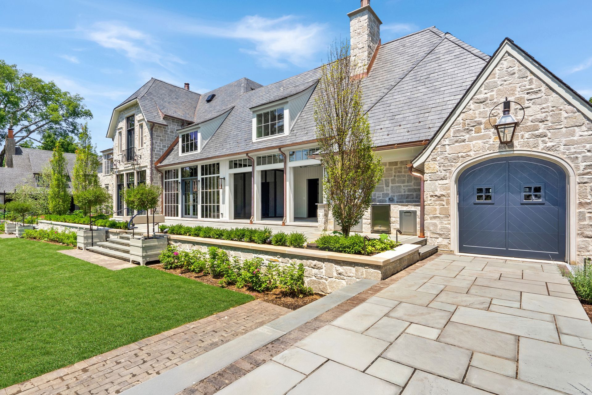 Luxury stone house with a gray roof, front porch, manicured lawn, and paved driveway