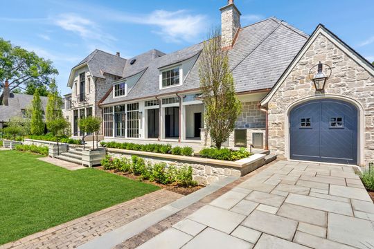 Stone suburban house with gray roof, front porch, manicured lawn, and single-car garage