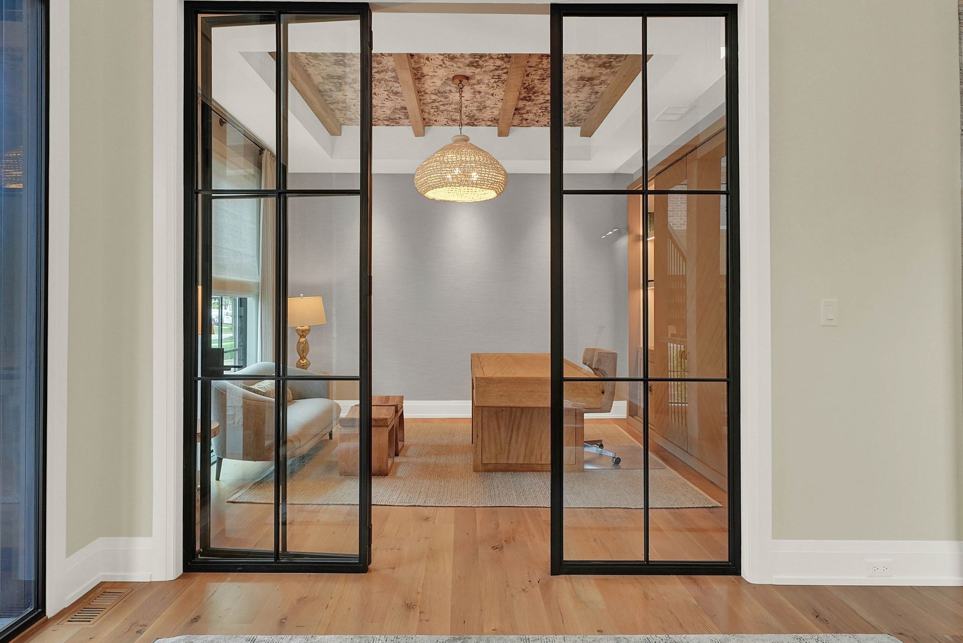 Black-framed glass double doors open to a bright room with a wood table, chairs, rug, and pendant light.