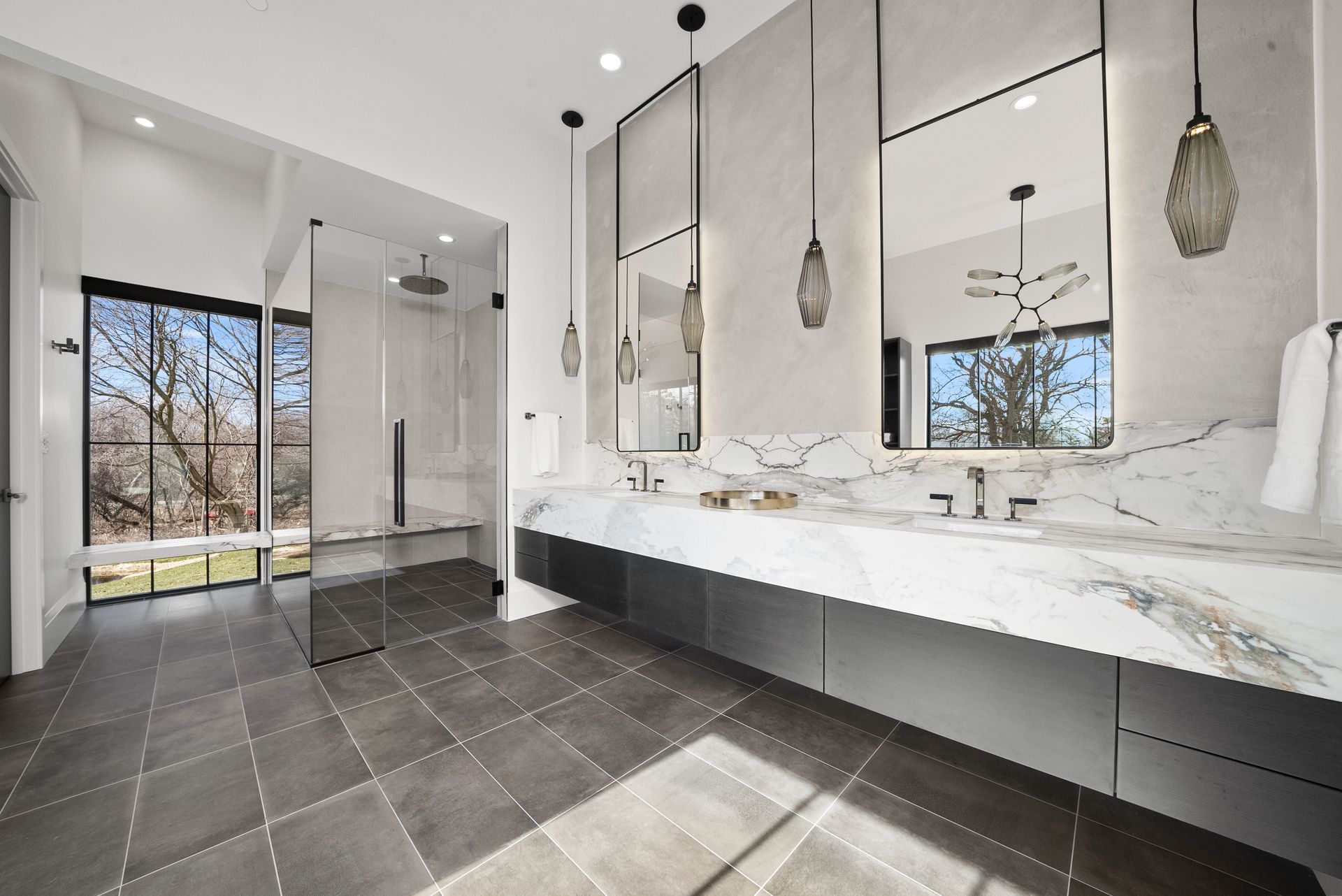 Modern bathroom with black marble floor, double vanity, large mirrors, and walk-in glass shower