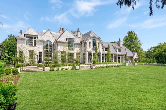 Large stone mansion with tall windows and a broad green lawn under a clear blue sky
