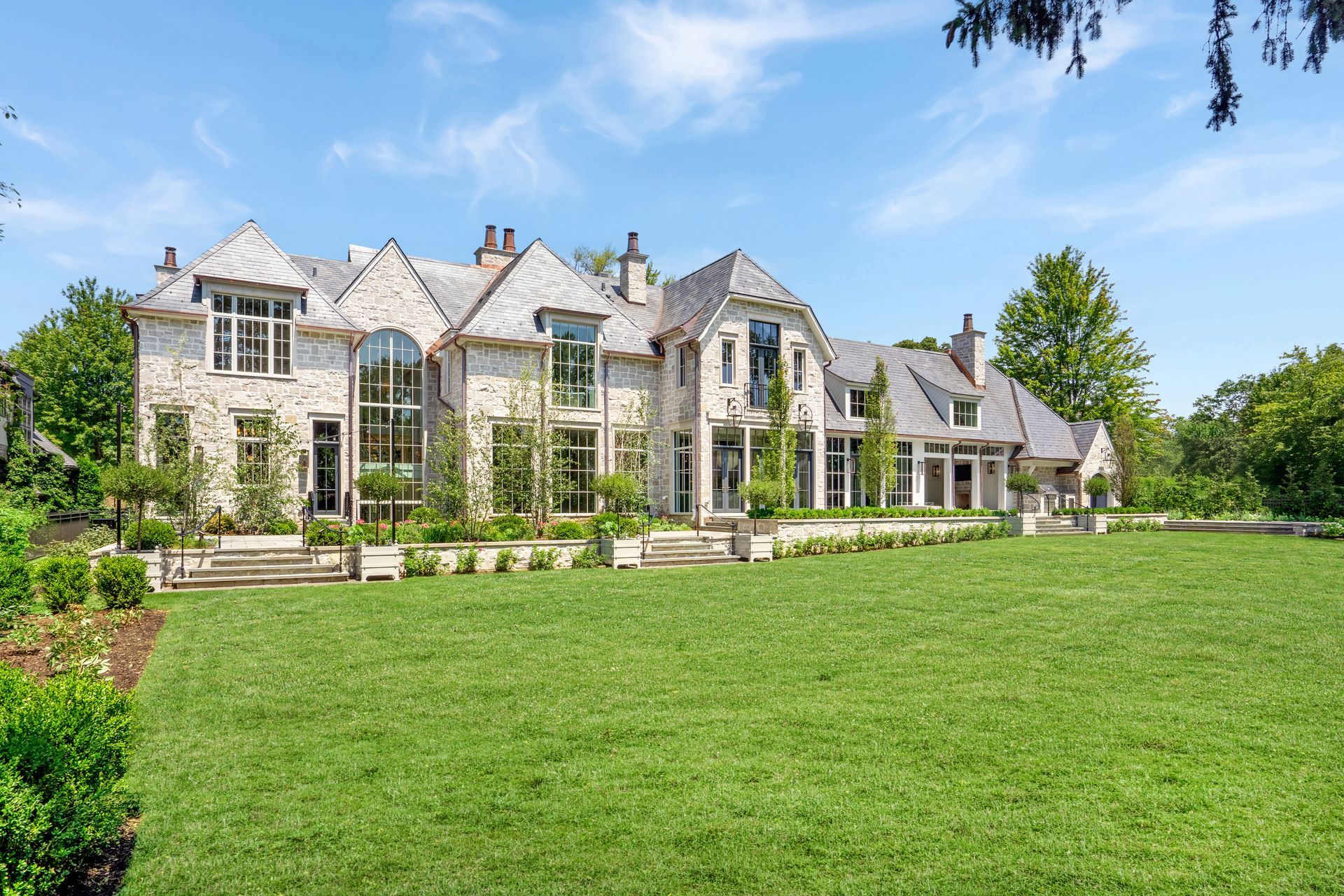 Large stone mansion with tall windows and a manicured green lawn under a blue sky