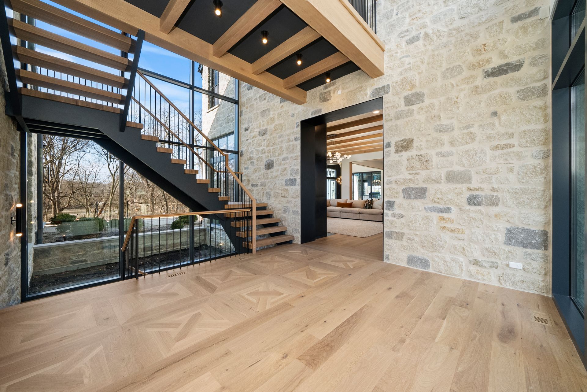 Modern open living space with wood floors, stone walls, and a floating staircase by large windows