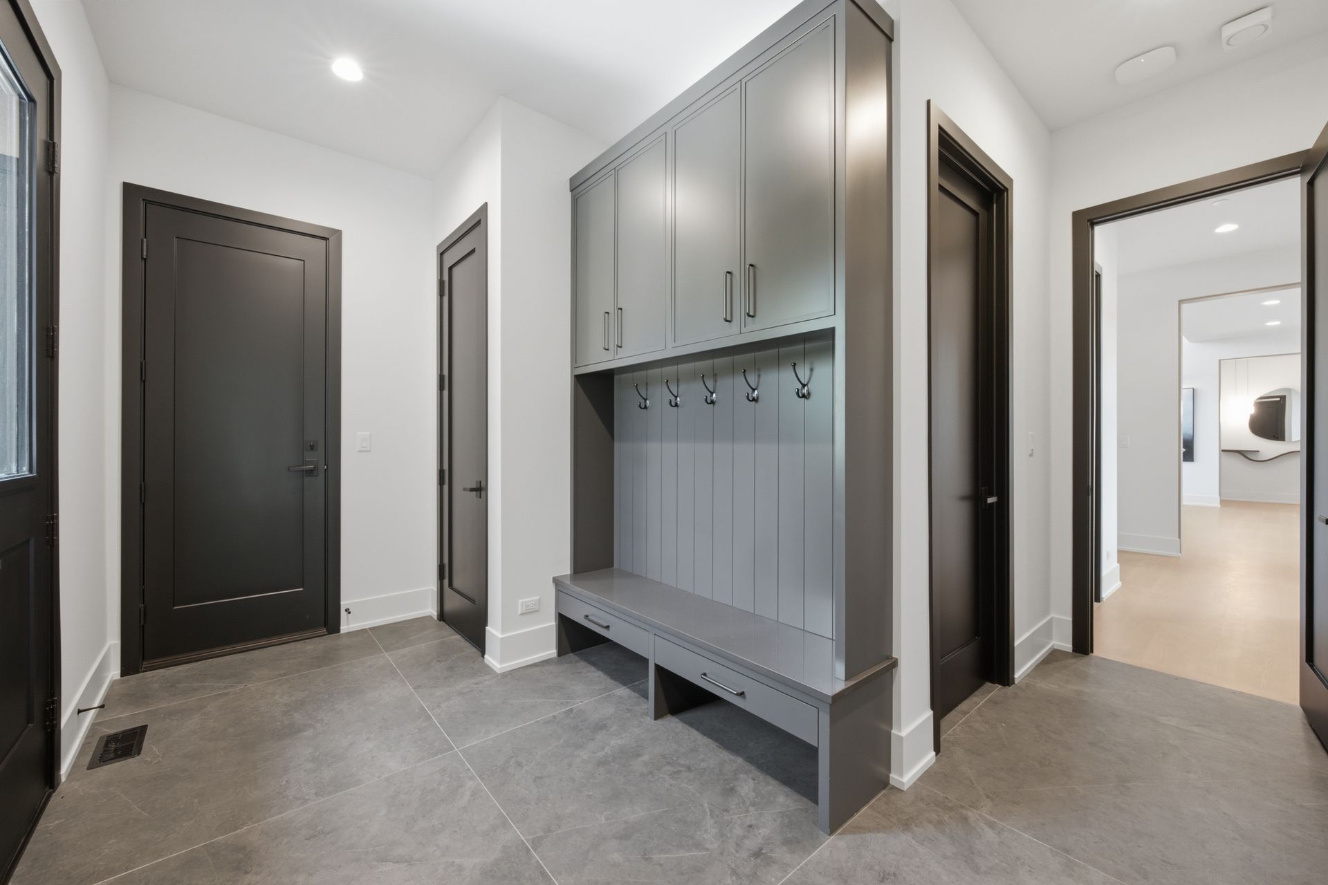 Modern hallway with gray tile floor, dark doors, and built-in gray coat hooks and cabinets.