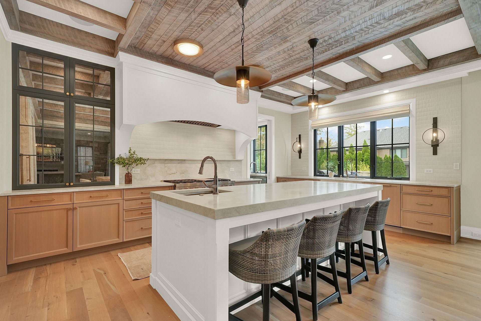 Bright modern kitchen with white island, wood cabinets, bar stools, and large windows
