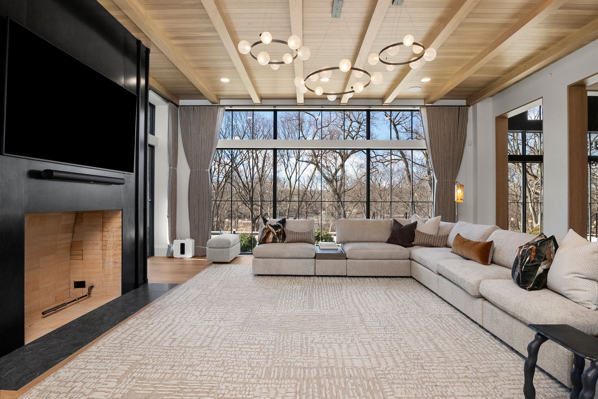 Modern living room with large sectional sofa, fireplace, and floor-to-ceiling window view of trees