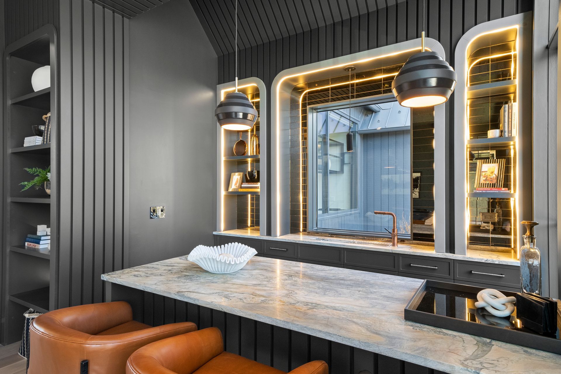 Modern barbershop with a large illuminated mirror, marble counter, and brown leather seating