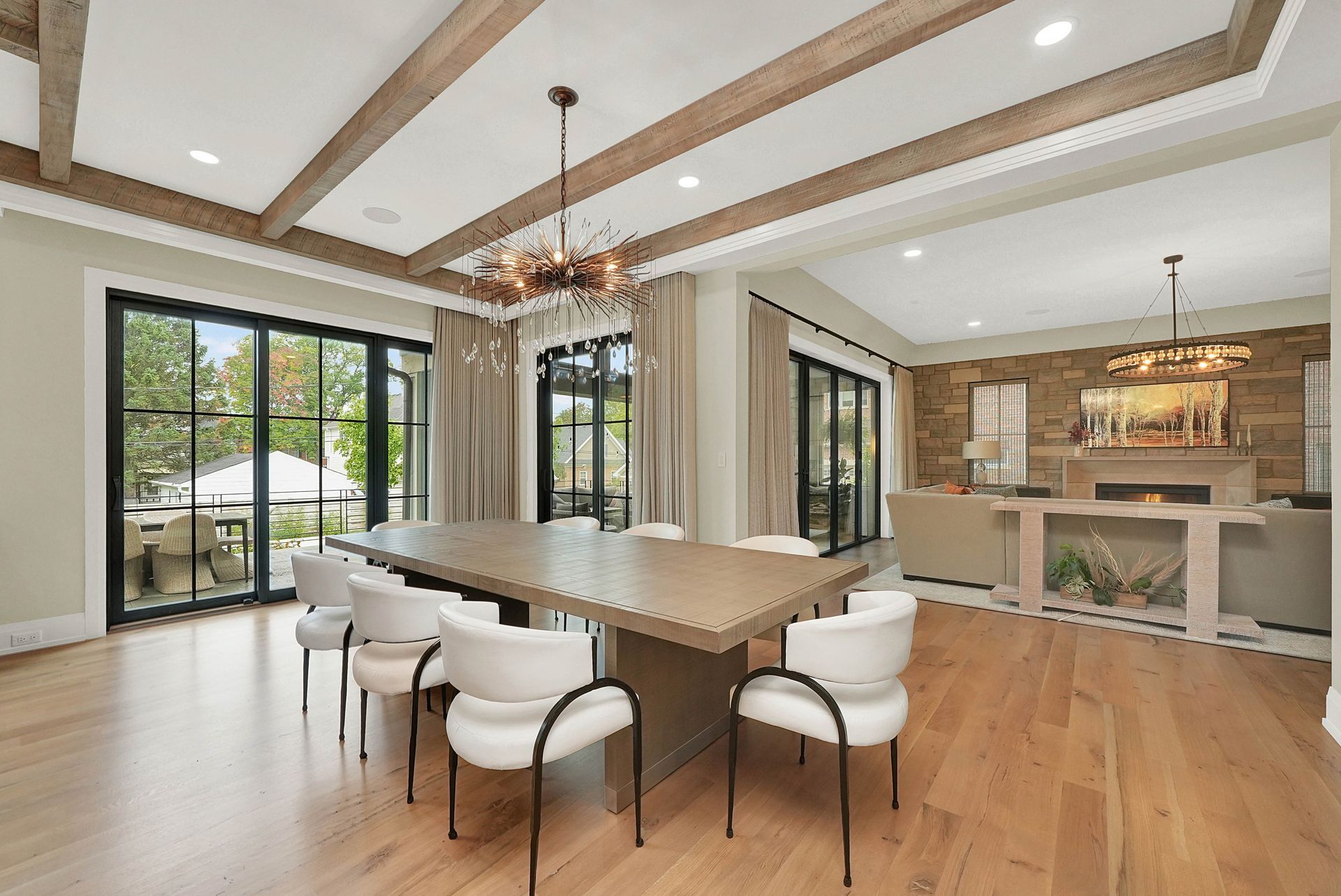 Modern open-concept dining room and kitchen with wood beams, large windows, and white chairs around a table