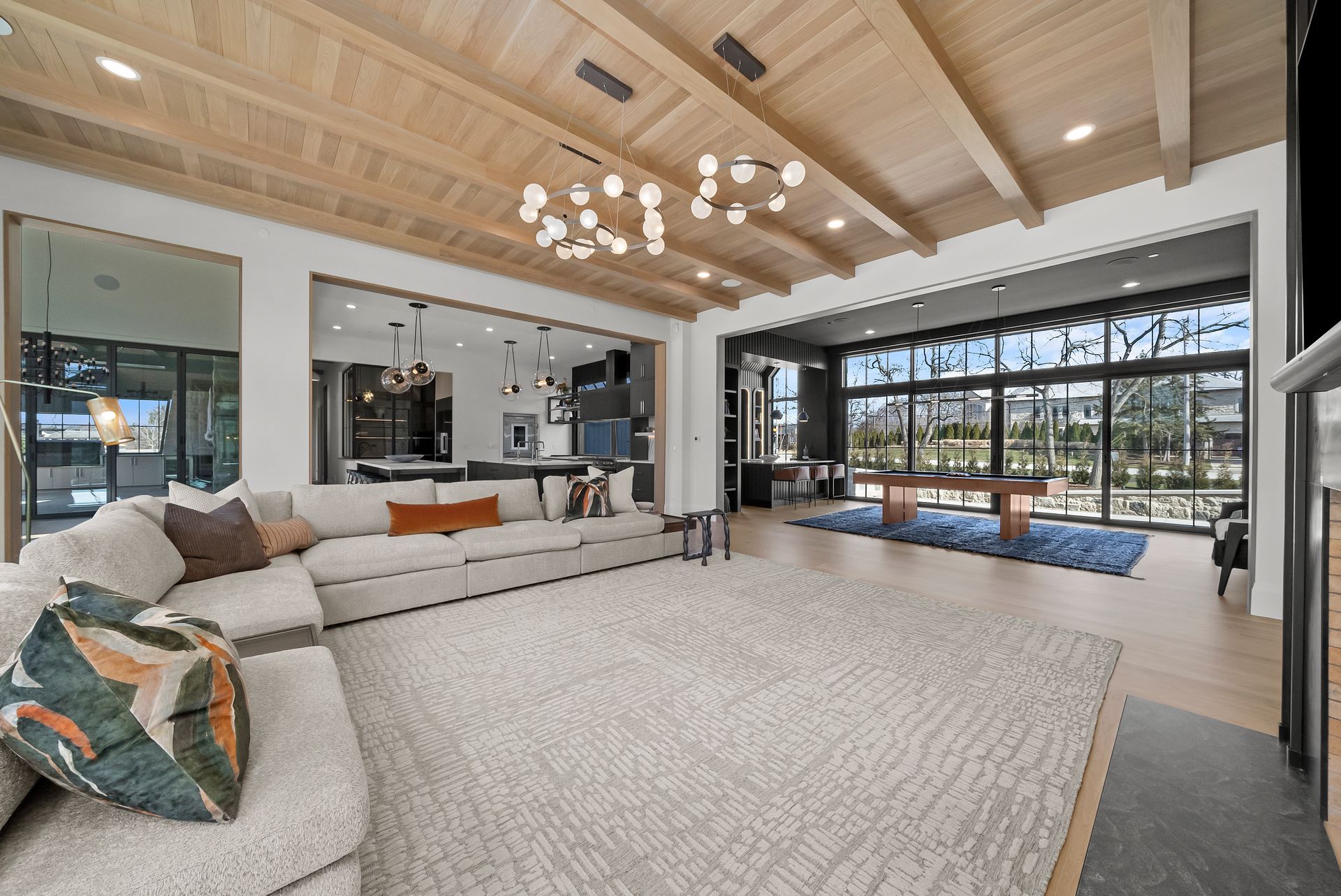 Spacious modern living room with vaulted wood ceiling, sectional sofa, rug, and large windows overlooking a patio.