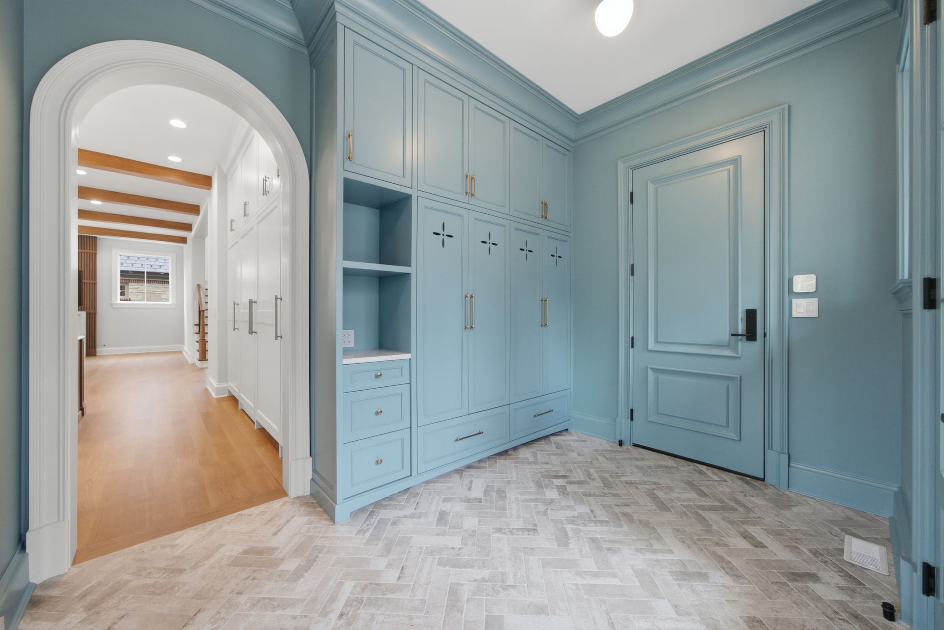 Light blue built-in mudroom with arched hallway, storage cabinets, and herringbone tile floor