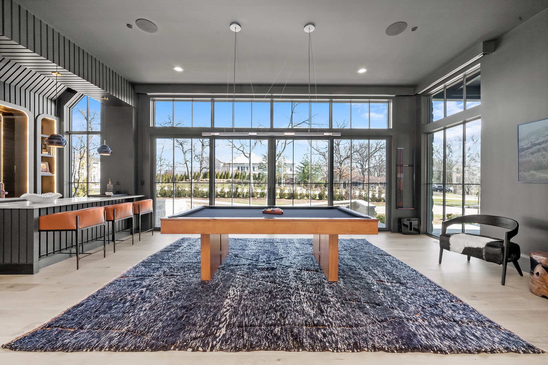Modern lobby with large windows, wooden table, blue rug, and pool table on the right