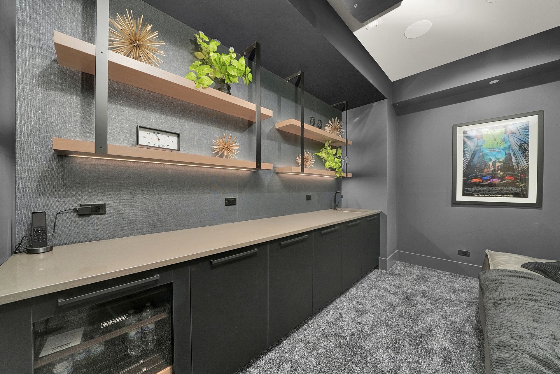 Modern gray home office with floating shelves, desk, carpet, and framed wall art.
