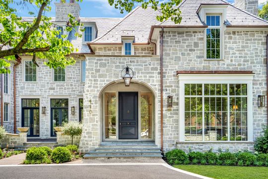 Stone house exterior with gray shutters, front door, and large window on a landscaped street