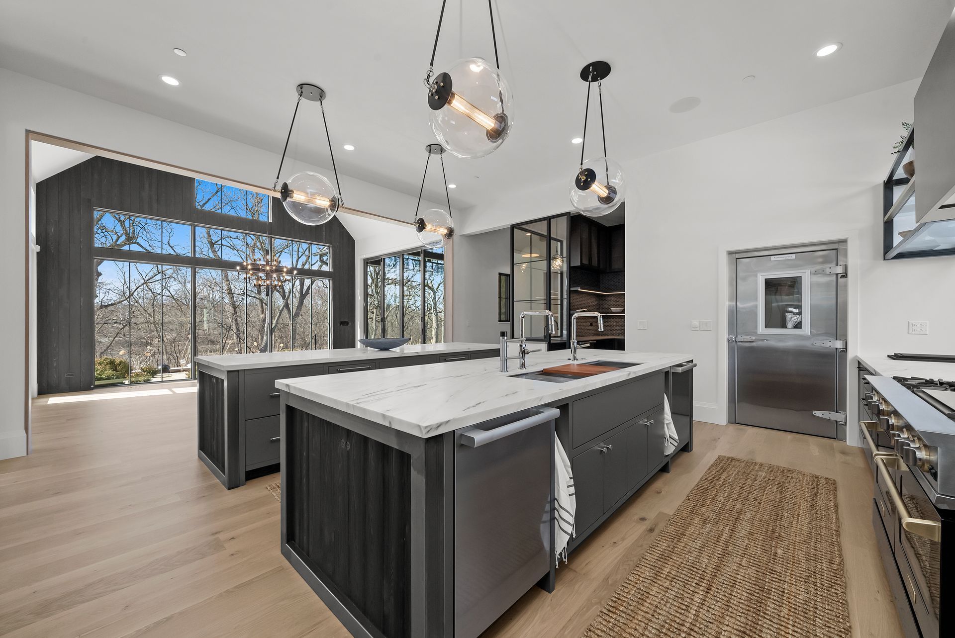 Modern kitchen with large windows, marble island, pendant lights, dark cabinets, and woven runner rug