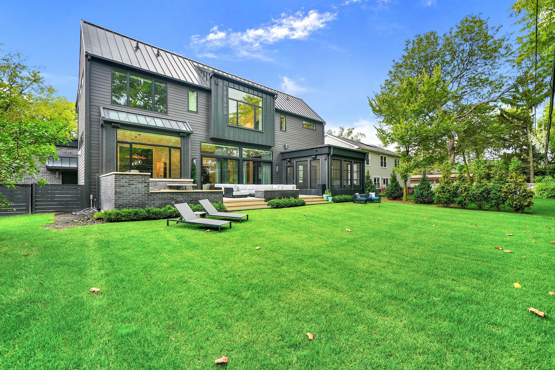 Modern dark-gray house with large windows and a spacious green lawn under a bright blue sky