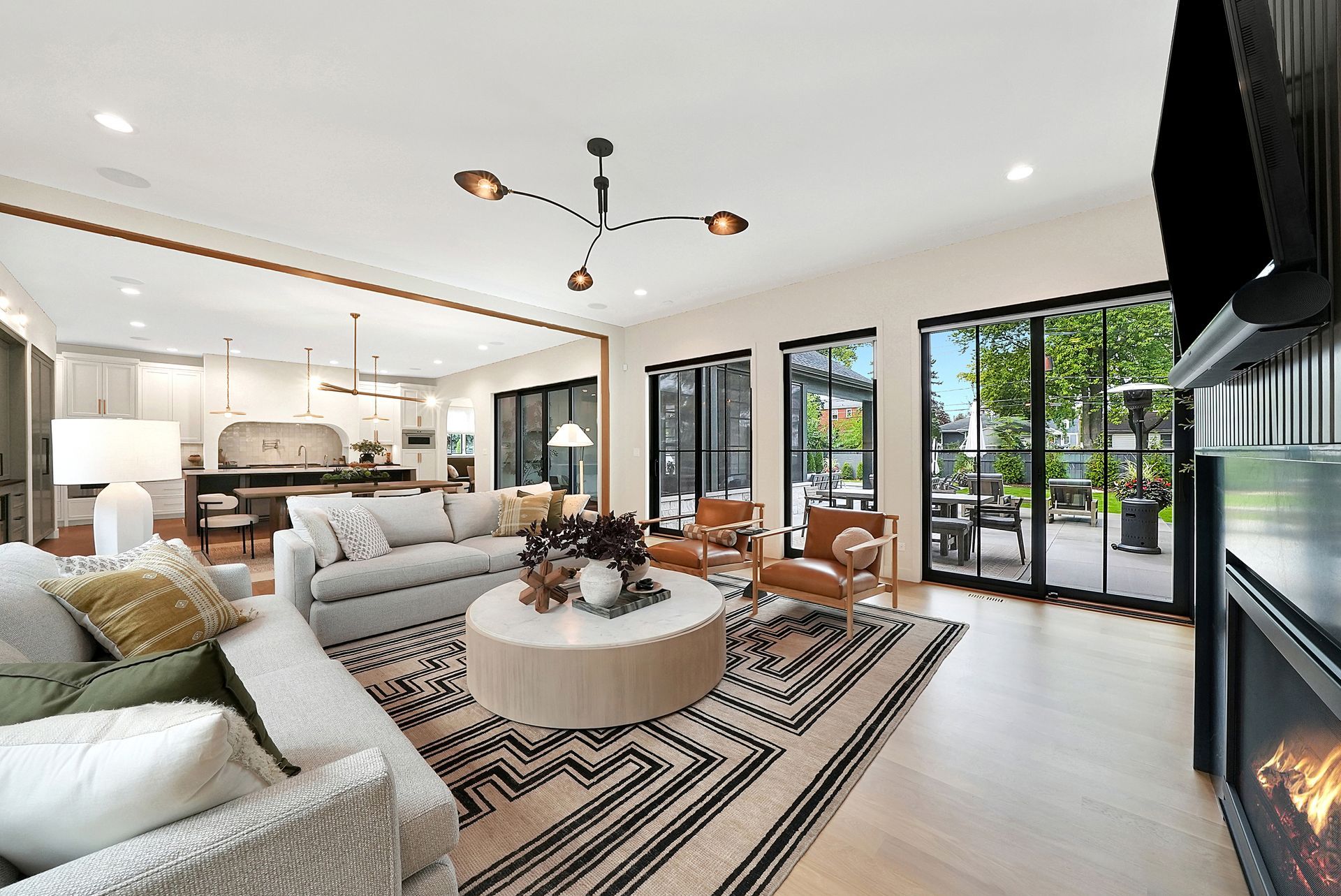 Bright open-plan living room with sofas, coffee table, fireplace, kitchen, and large windows.