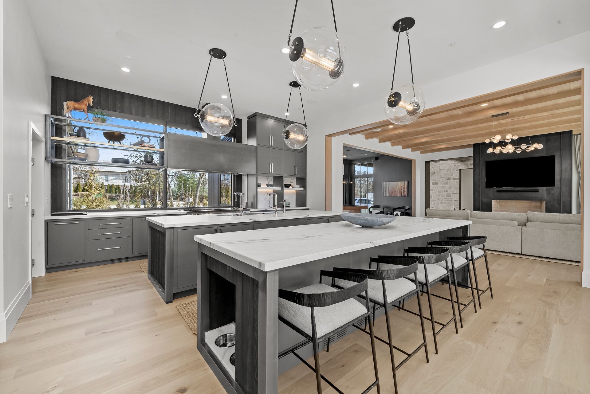 Modern open-concept kitchen with gray cabinets, wood floors, large island, and pendant lights