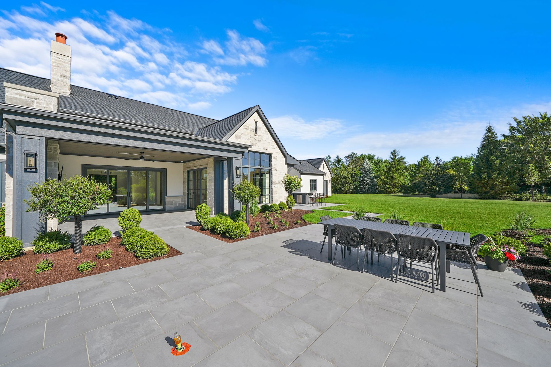 Modern patio with outdoor dining set beside a white house and lawn under a bright blue sky