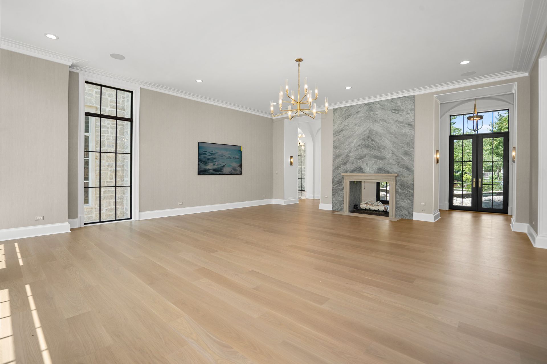 Bright empty living room with wood floors, chandelier, fireplace, and tall windows