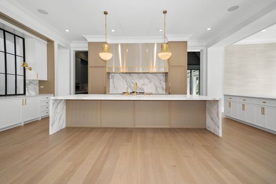 Modern kitchen with large marble island, light wood cabinets, pendant lights, and oak floors