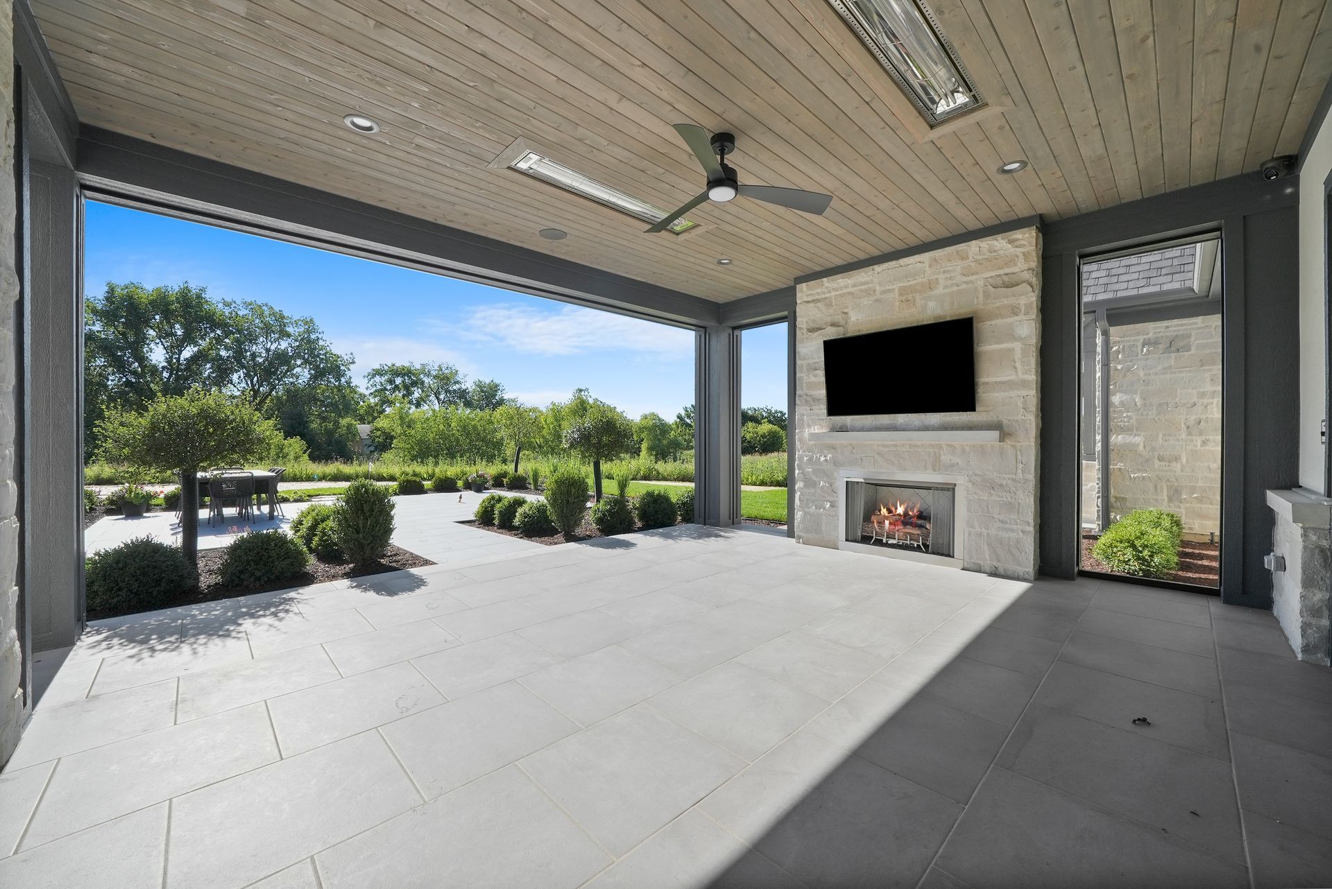 Covered patio with TV and fireplace overlooking a landscaped yard