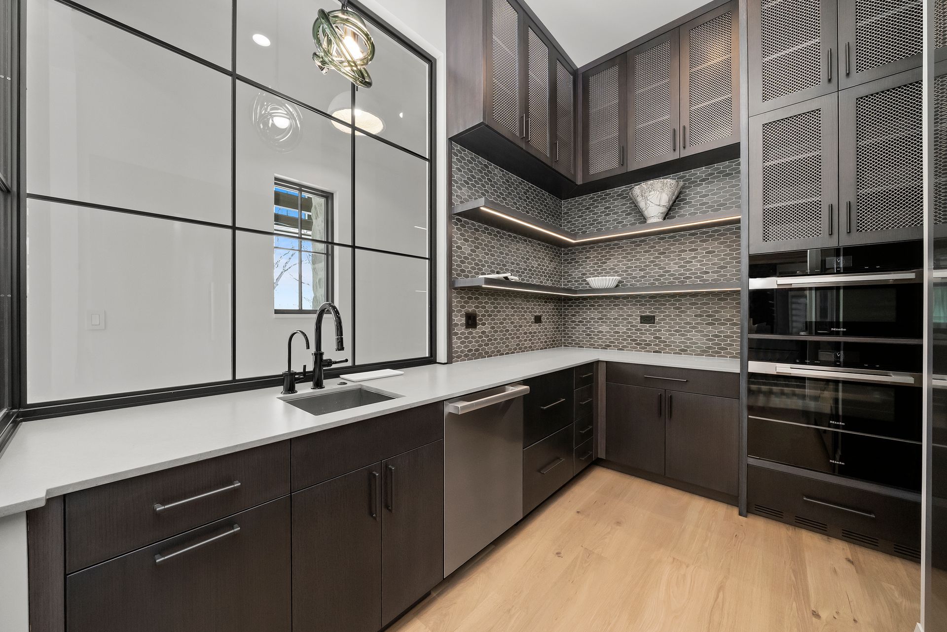 Modern kitchen with dark cabinets, white countertops, mirrored wall cabinets, and wood flooring