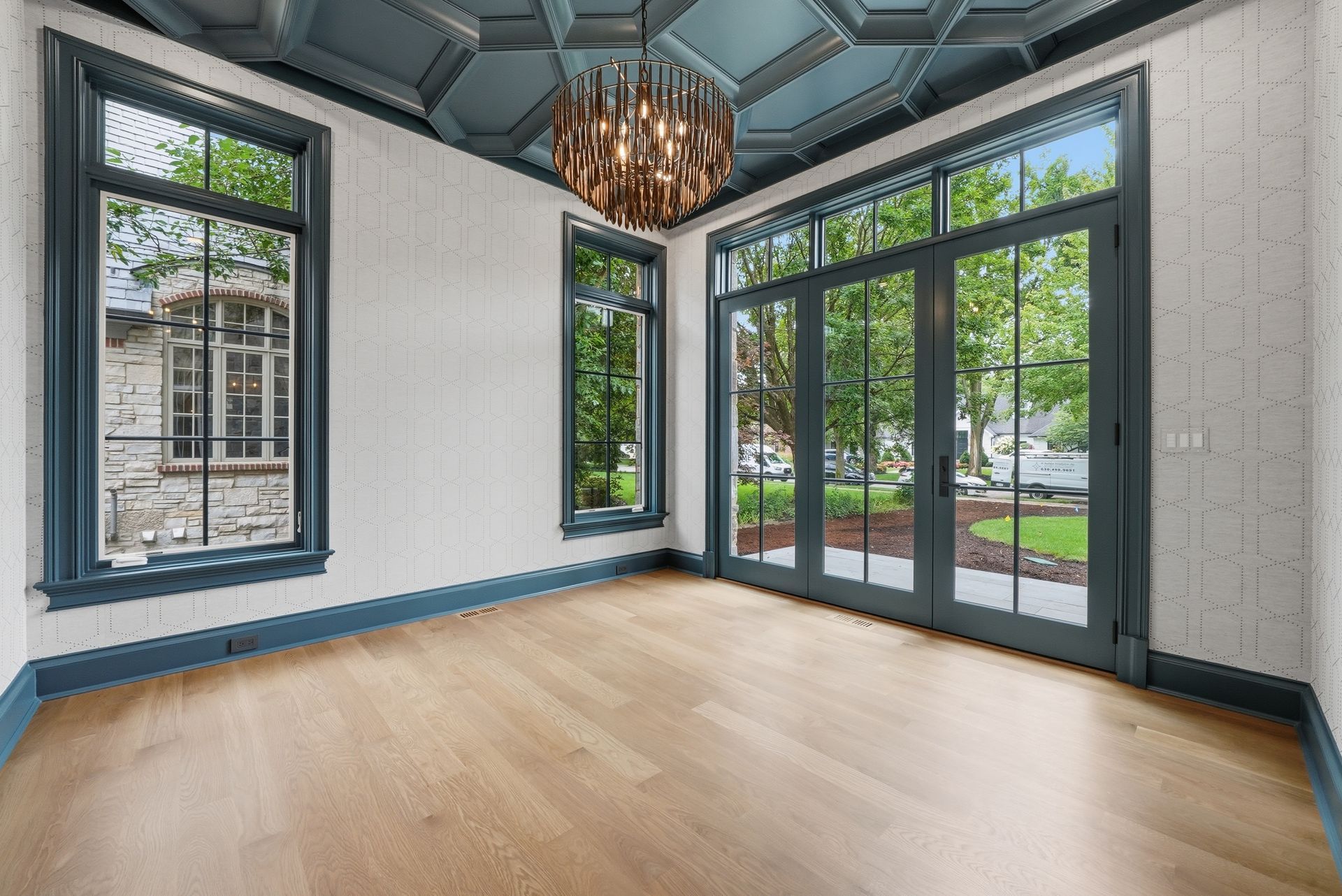 Bright empty room with large windows, glass doors, light wood floors, and a chandelier