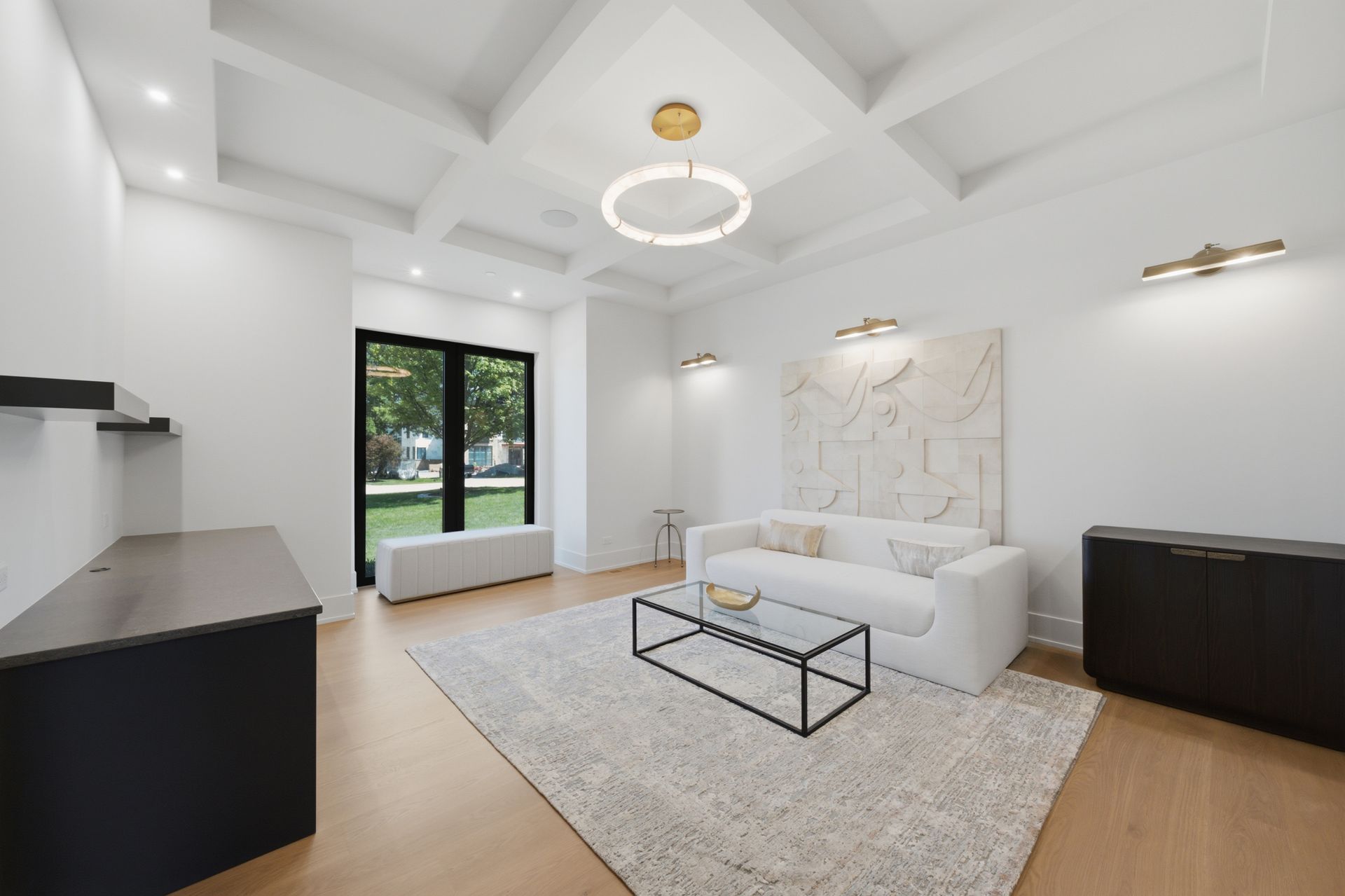 Bright modern living room with white sofa, black coffee table, rug, and large window with garden view