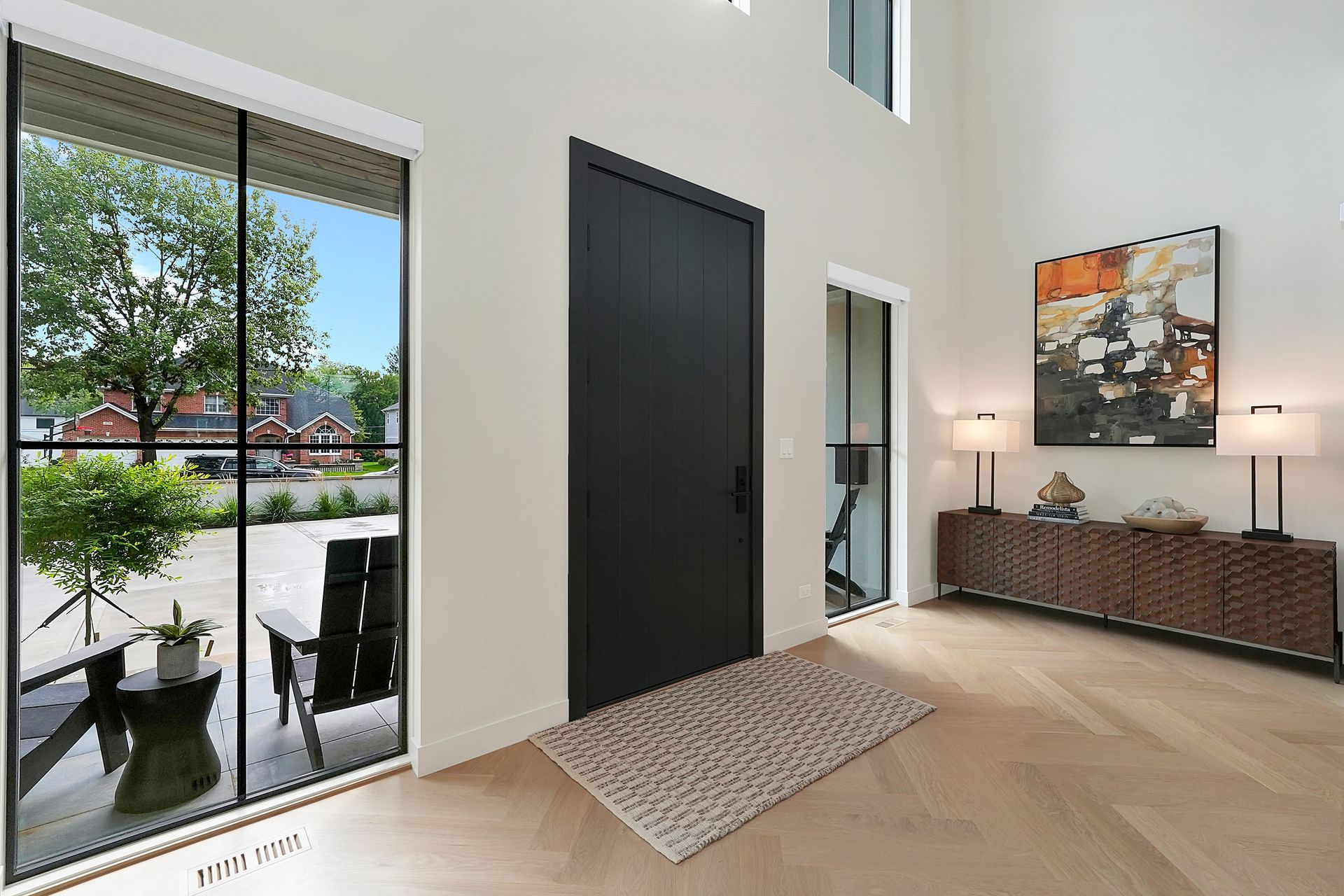 Modern entryway with black front door, floor-to-ceiling windows, console table, lamp, and wall art