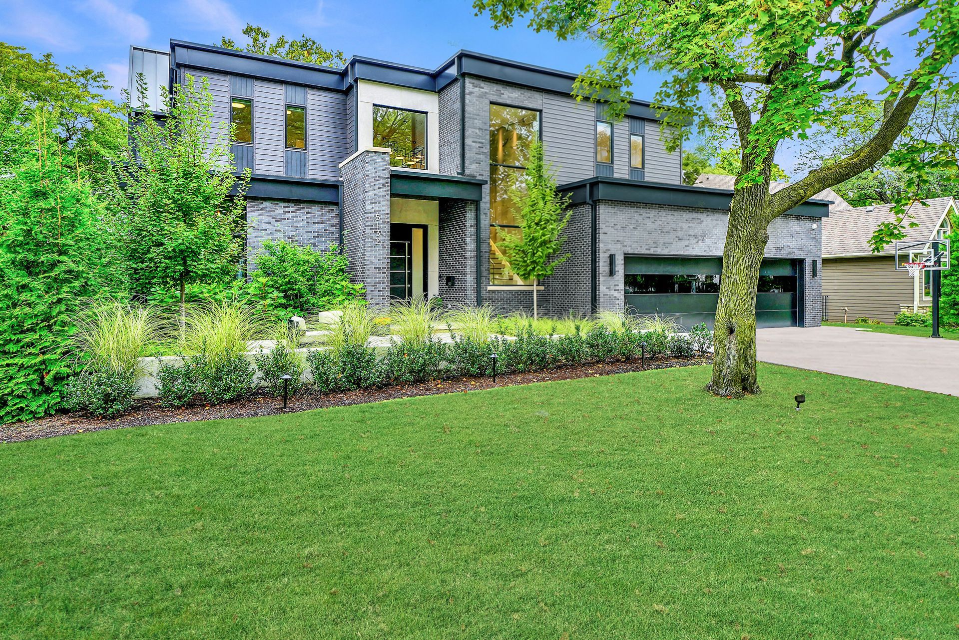 Modern two-story house with stone facade, green lawn, and driveway under leafy trees